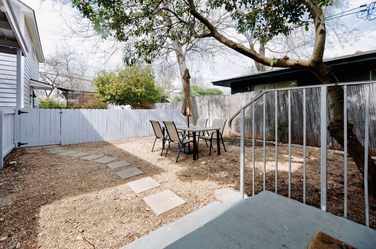 Panoramic view of a long winding dirt path with metal railings leading through trees and residential buildings.