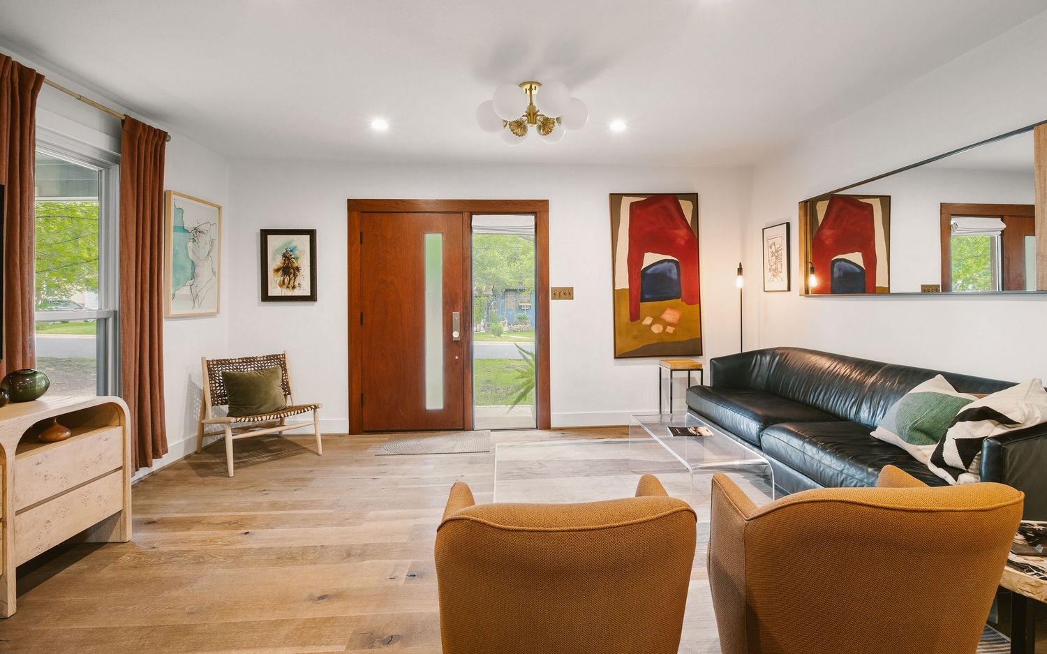 Modern living room with leather sofa, mustard chairs, hardwood floors, and a wood front door with natural light.