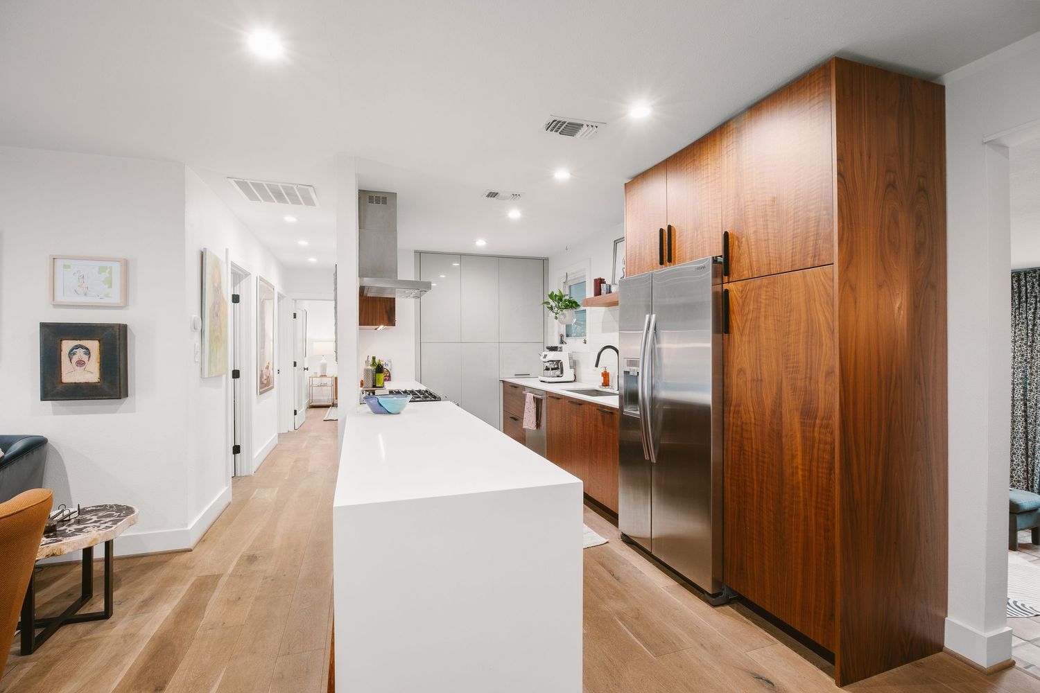 Modern kitchen with walnut cabinets, white island, stainless steel fridge, and light hardwood floors in open layout.