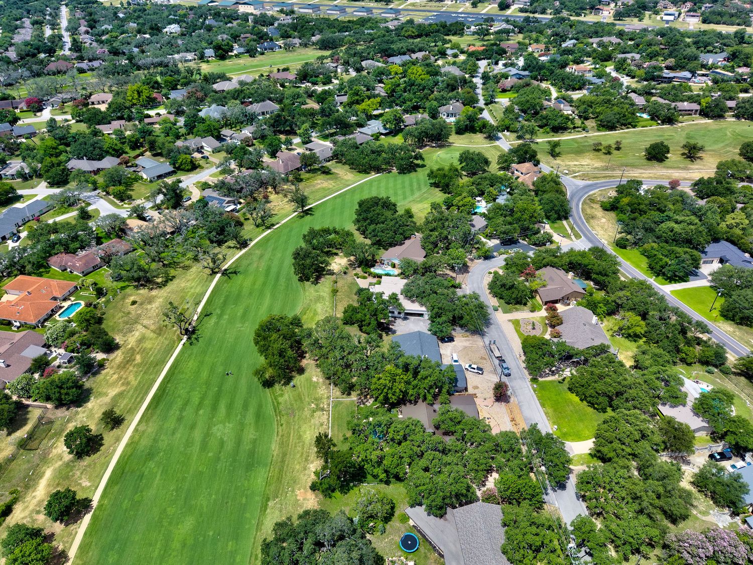 Aerial view of a lush suburban neighborhood with green golf course fairway, tree-lined streets, and residential homes in Texas.
