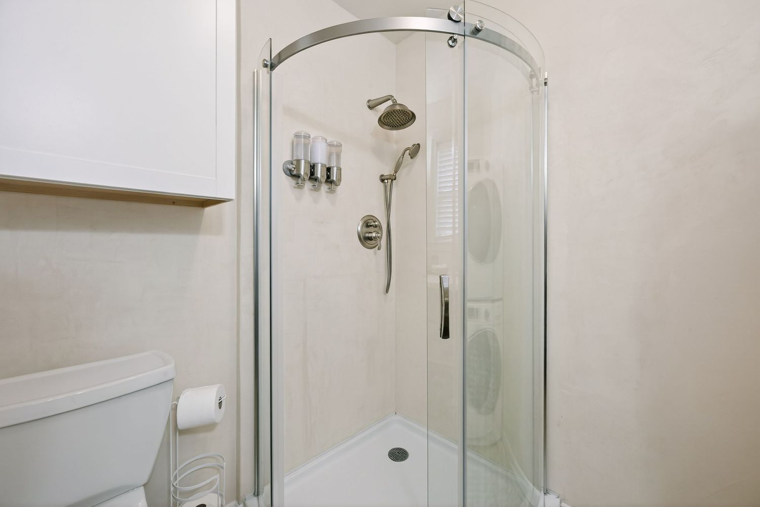 Modern bathroom interior with curved glass shower enclosure, chrome fixtures and white tile walls.
