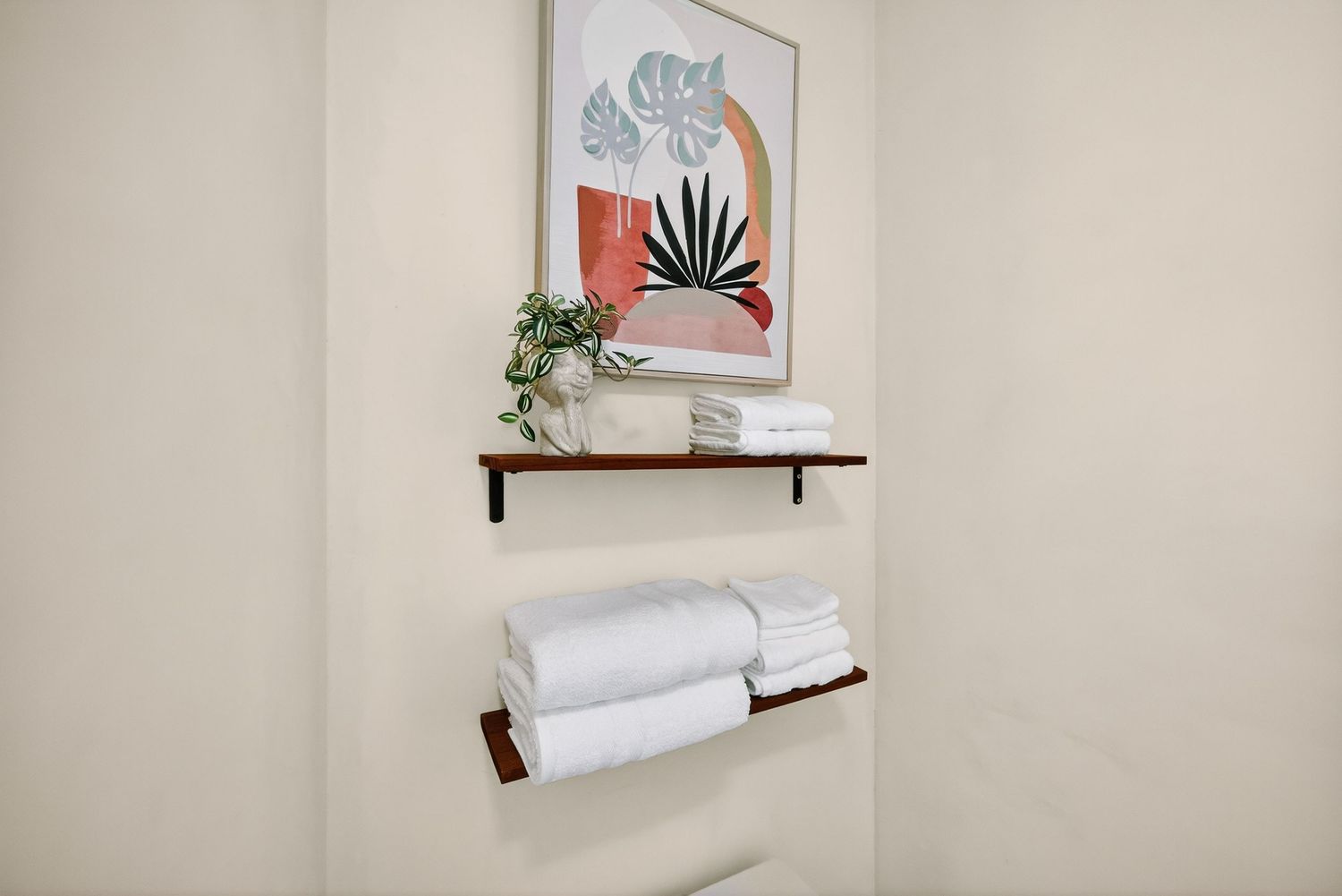 White towel rolls displayed on minimalist floating wooden shelves against a beige wall with decorative artwork.
