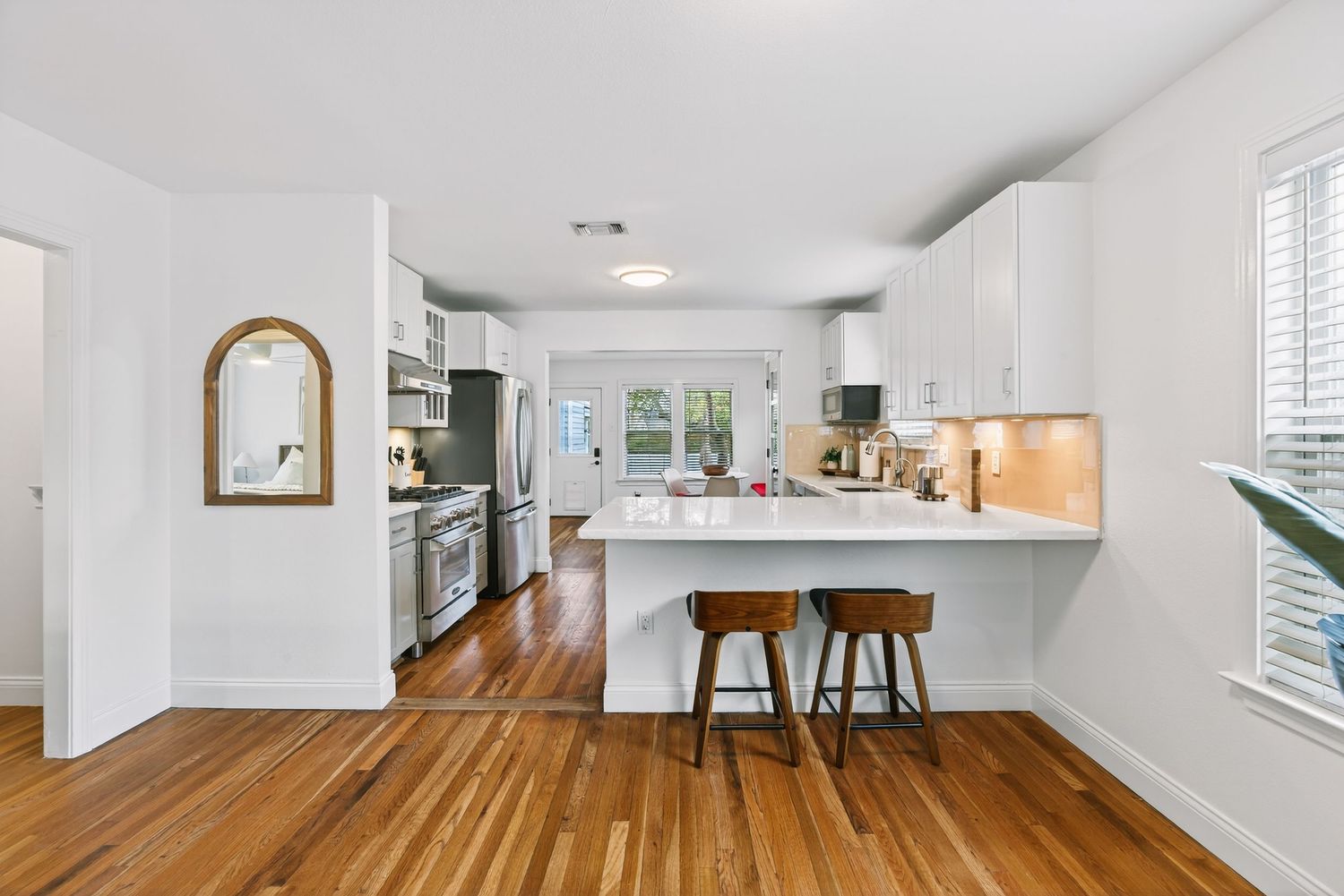 Modern white kitchen with hardwood floors, stainless steel appliances, and a peninsula with wooden bar stools.