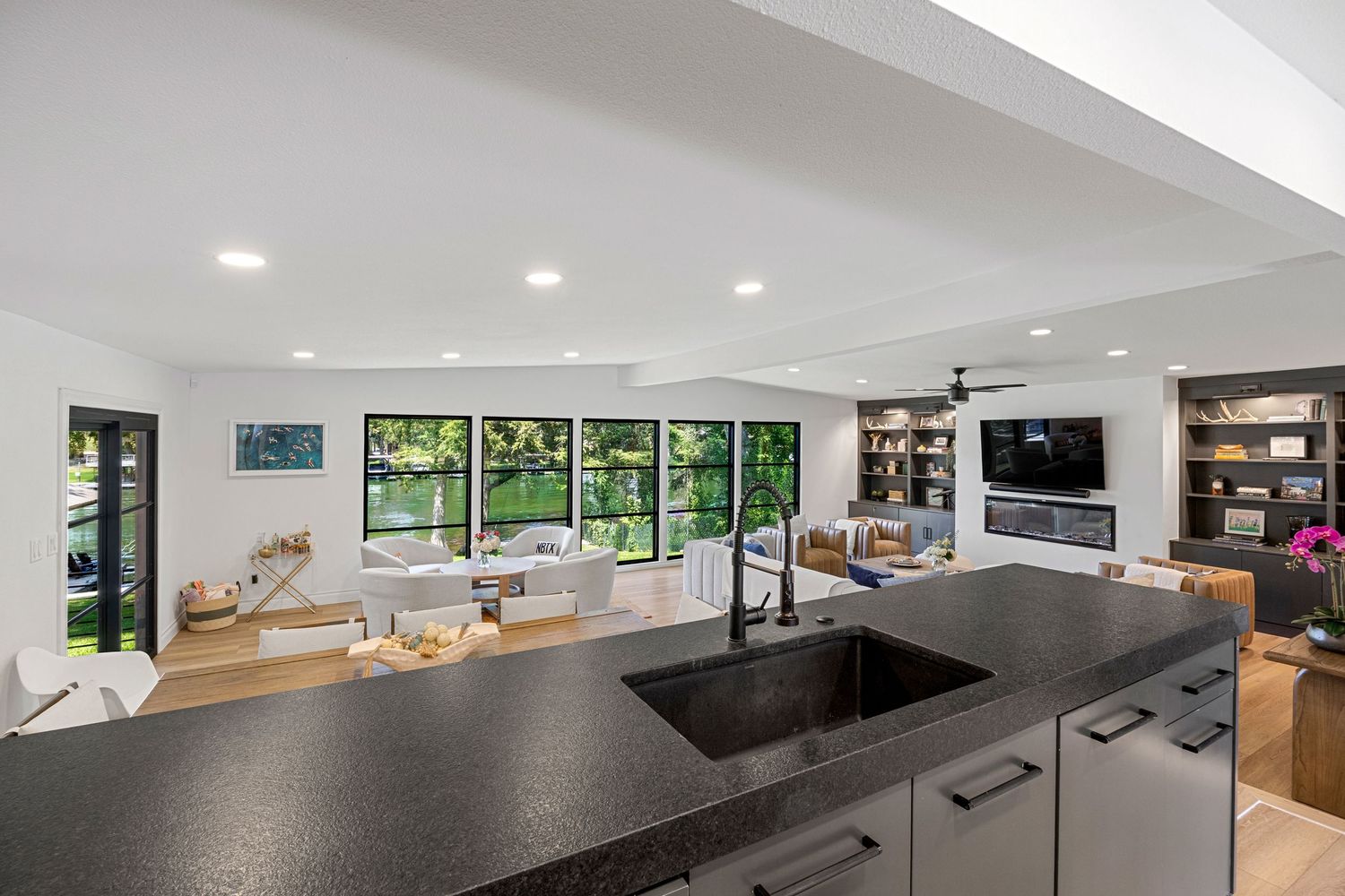 Modern kitchen with dark granite island, undermount sink, and open view into bright living area with large garden windows.