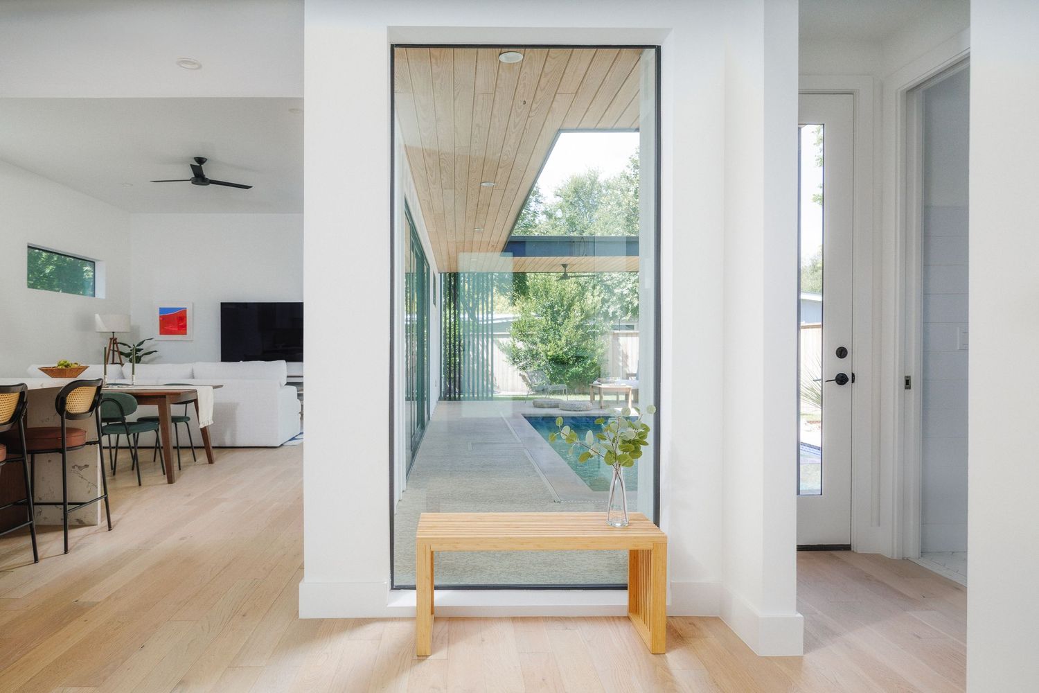 Modern minimalist interior hallway with white walls, wooden flooring and natural light streaming through windows.