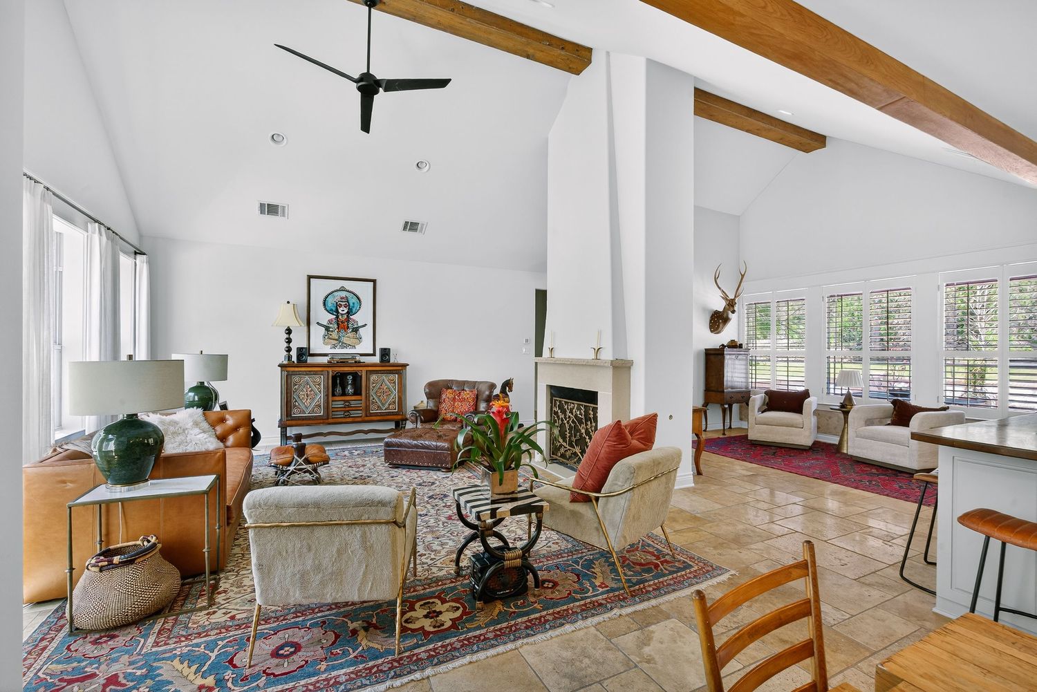 Spacious living room with vaulted ceilings, exposed wood beams, a fireplace, and a colorful area rug on tile floors.