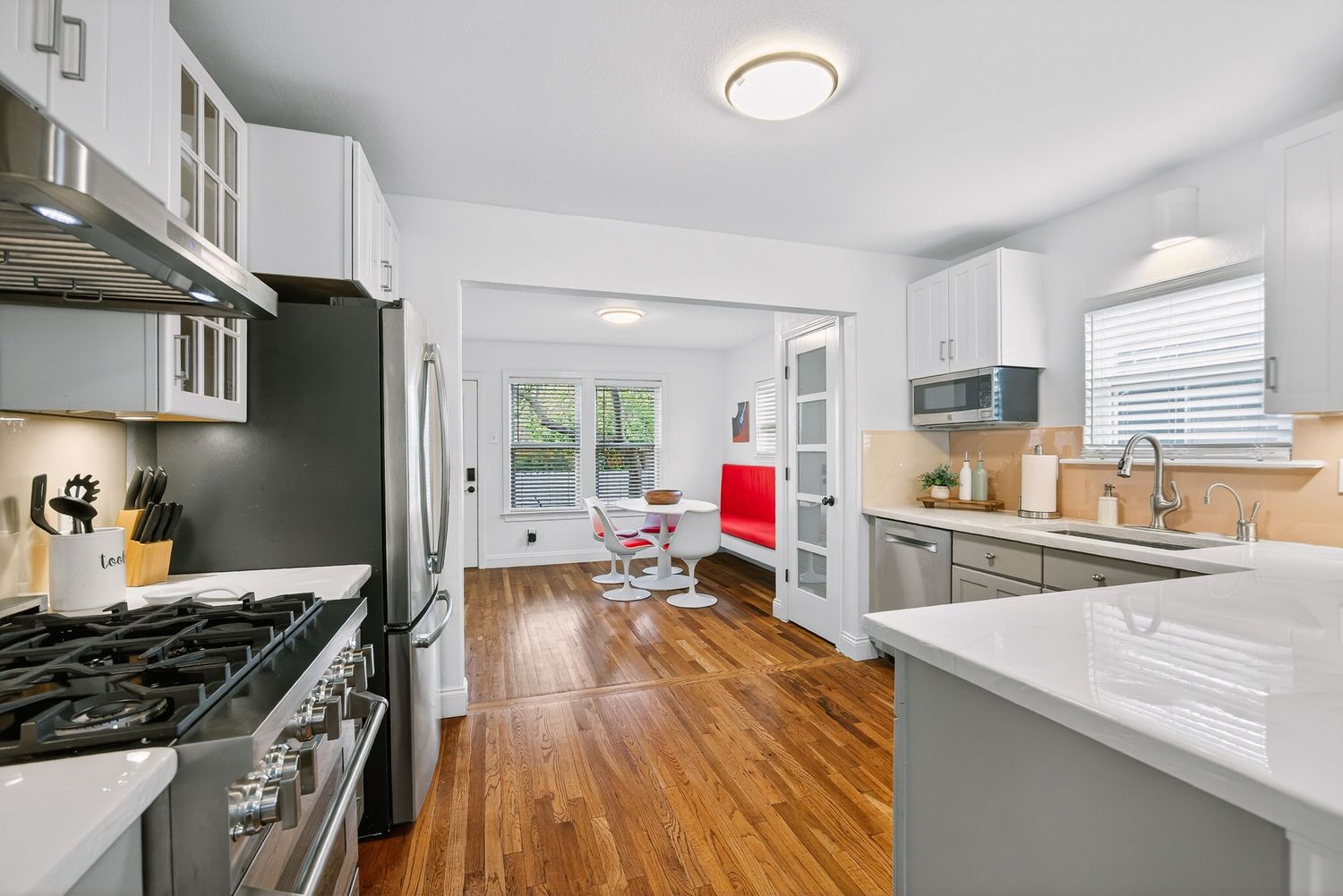 A modern kitchen and living room space with hardwood floors, white cabinets, and recessed lighting creates an open concept layout.