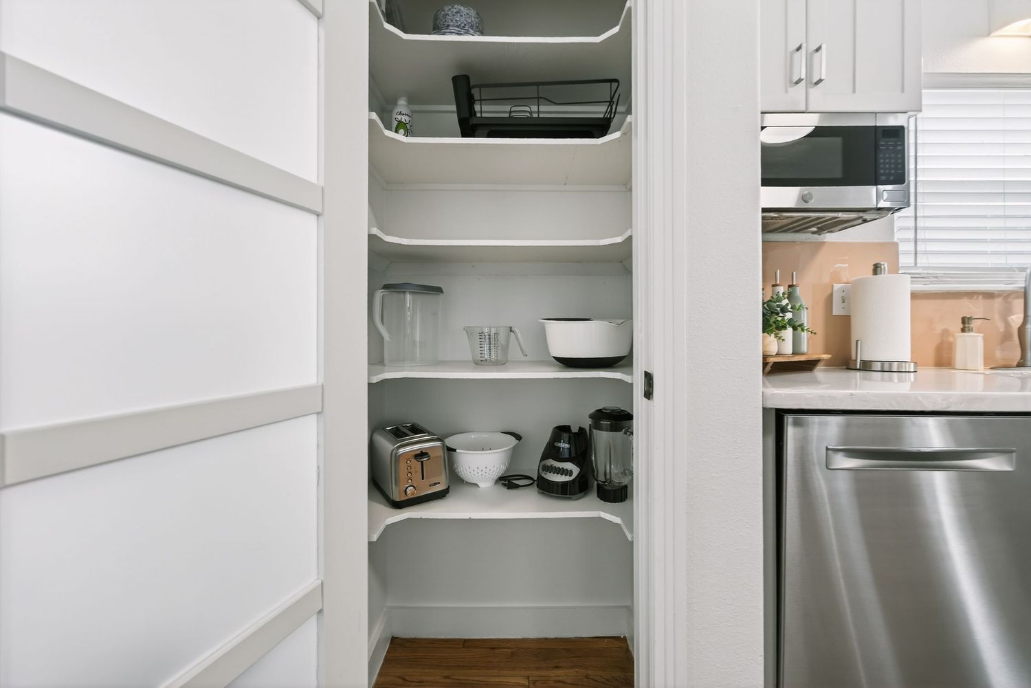 A modern white corner pantry with built-in shelving displays kitchenware, dishes and storage containers in an organized manner.