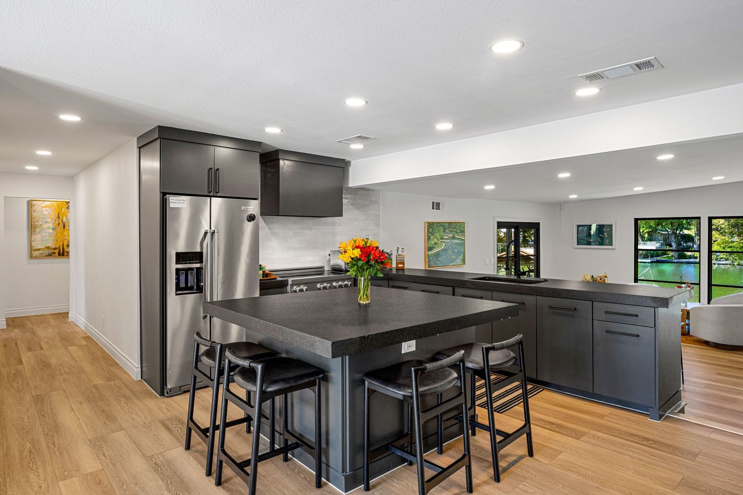 Contemporary kitchen with dark gray cabinetry, black island with bar seating, stainless steel fridge, and light hardwood floors.