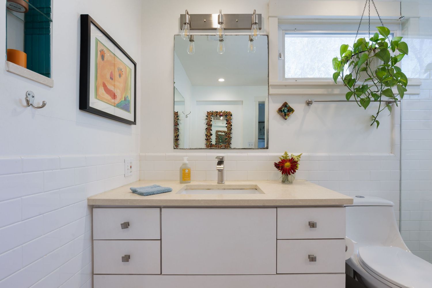 Contemporary white bathroom with floating vanity, large mirror, and hanging plant decor.