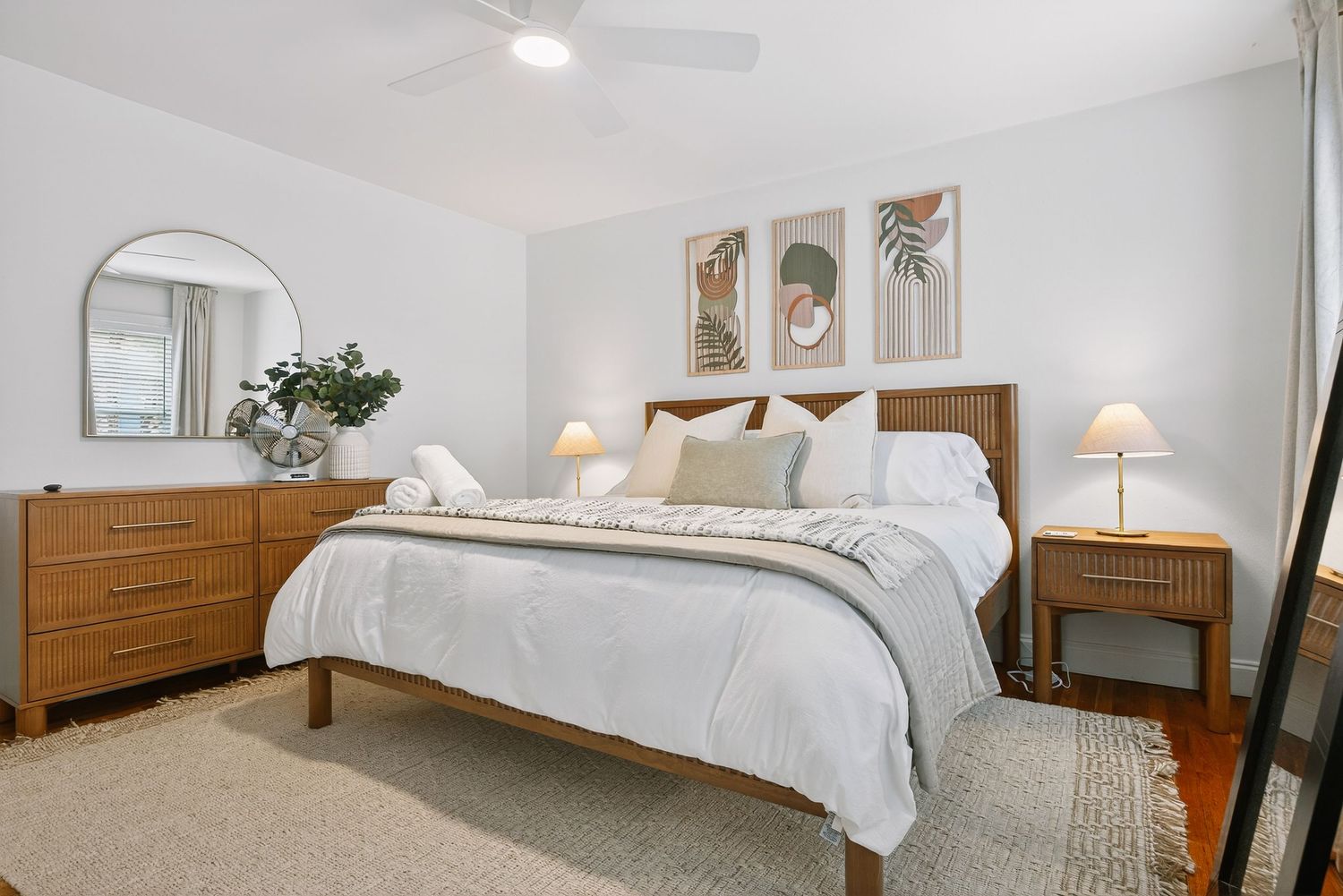 Bright and spacious bedroom with white bedding, wooden furniture, and natural light streaming through the window.
