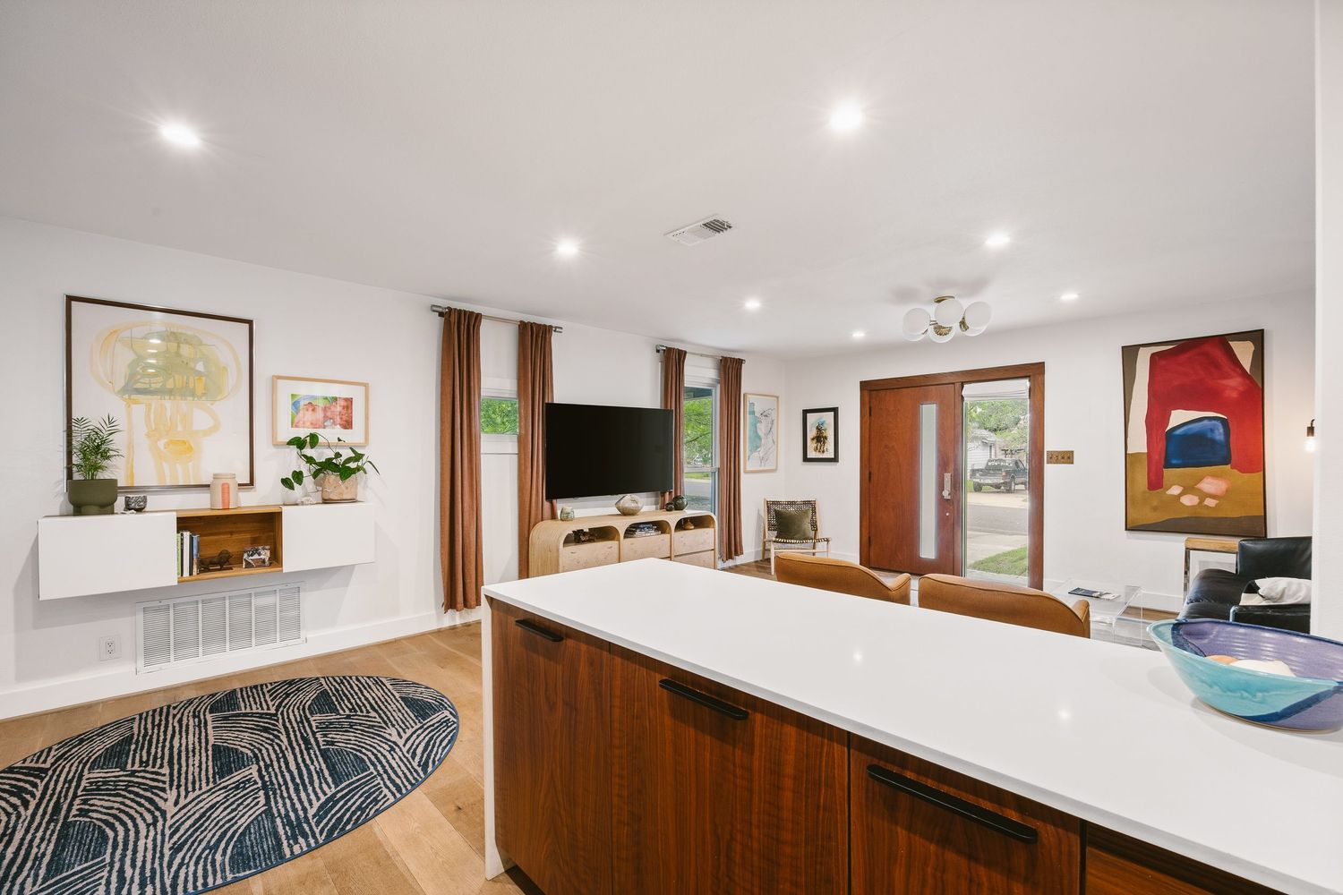Modern open-concept kitchen with white quartz island, walnut cabinets, and bright living room with hardwood floors and patio doors.