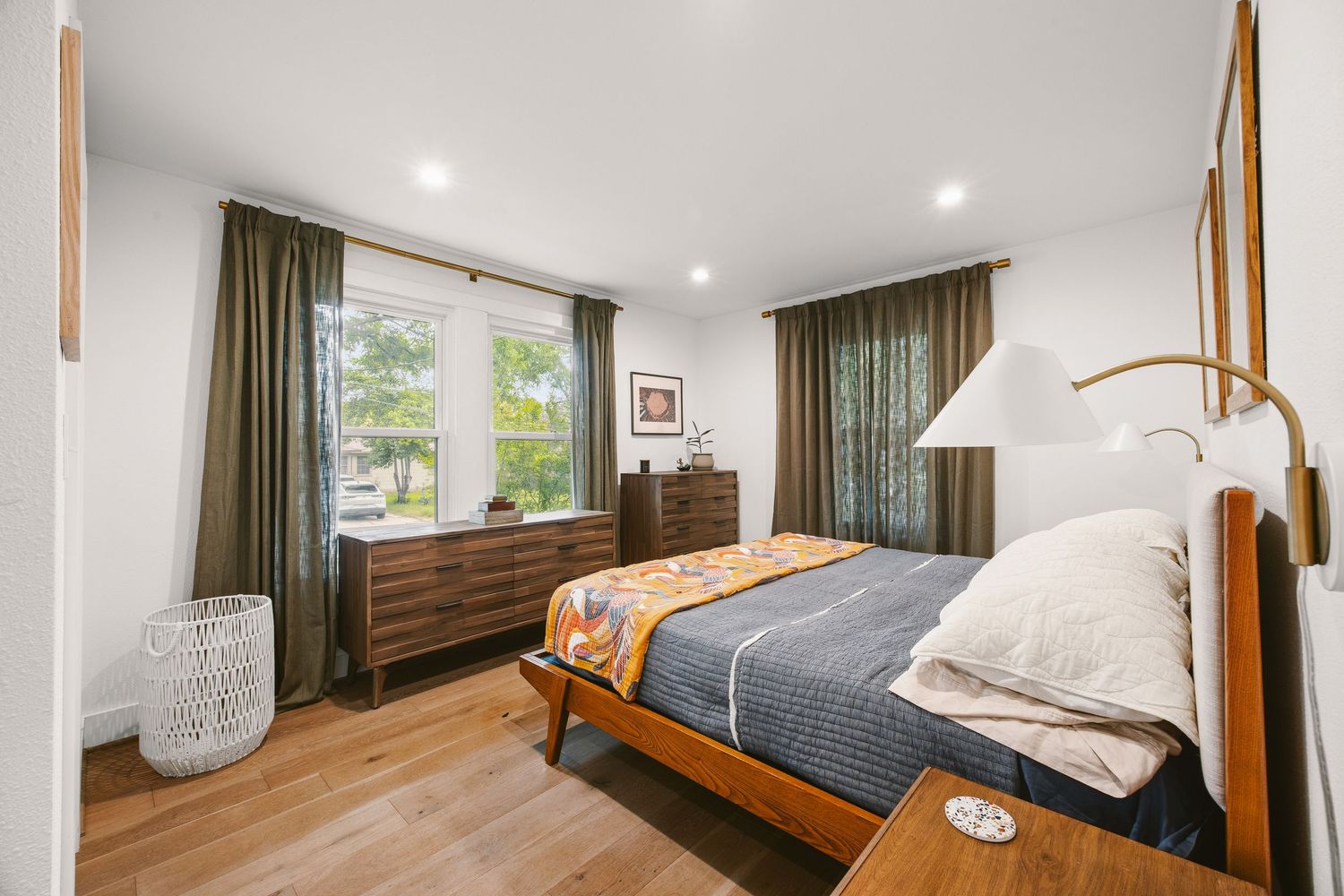 Mid-century modern bedroom with wood furniture, green curtains, hardwood floors, and natural light from large window.