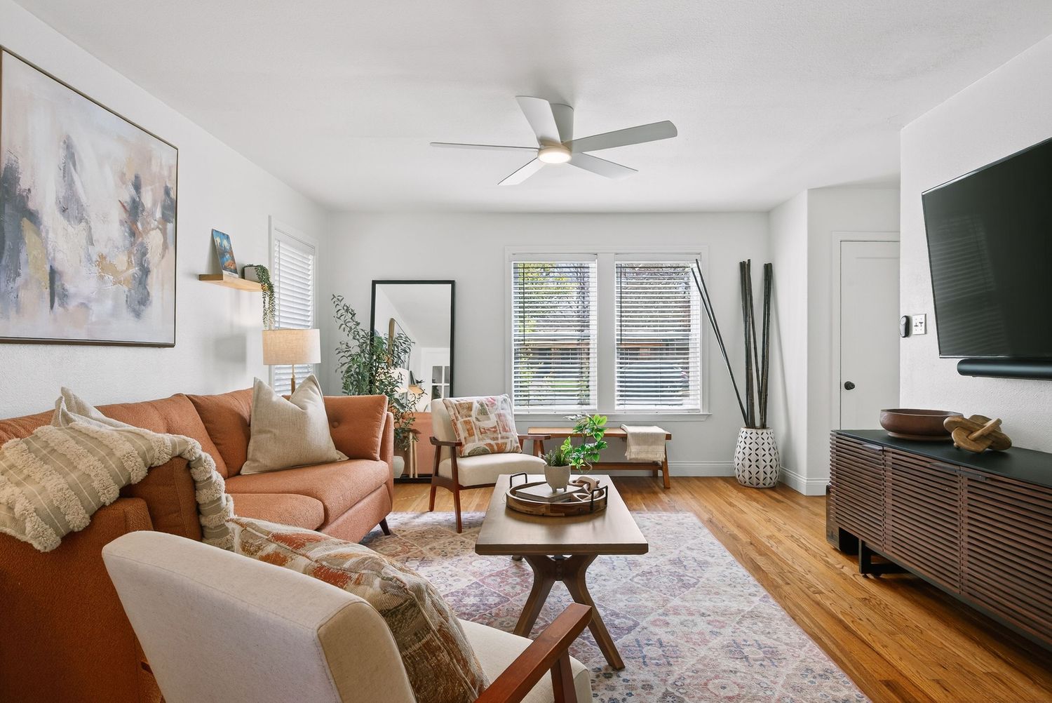 Modern living room with brown leather sofa, white walls, wood flooring and large windows letting in natural light.