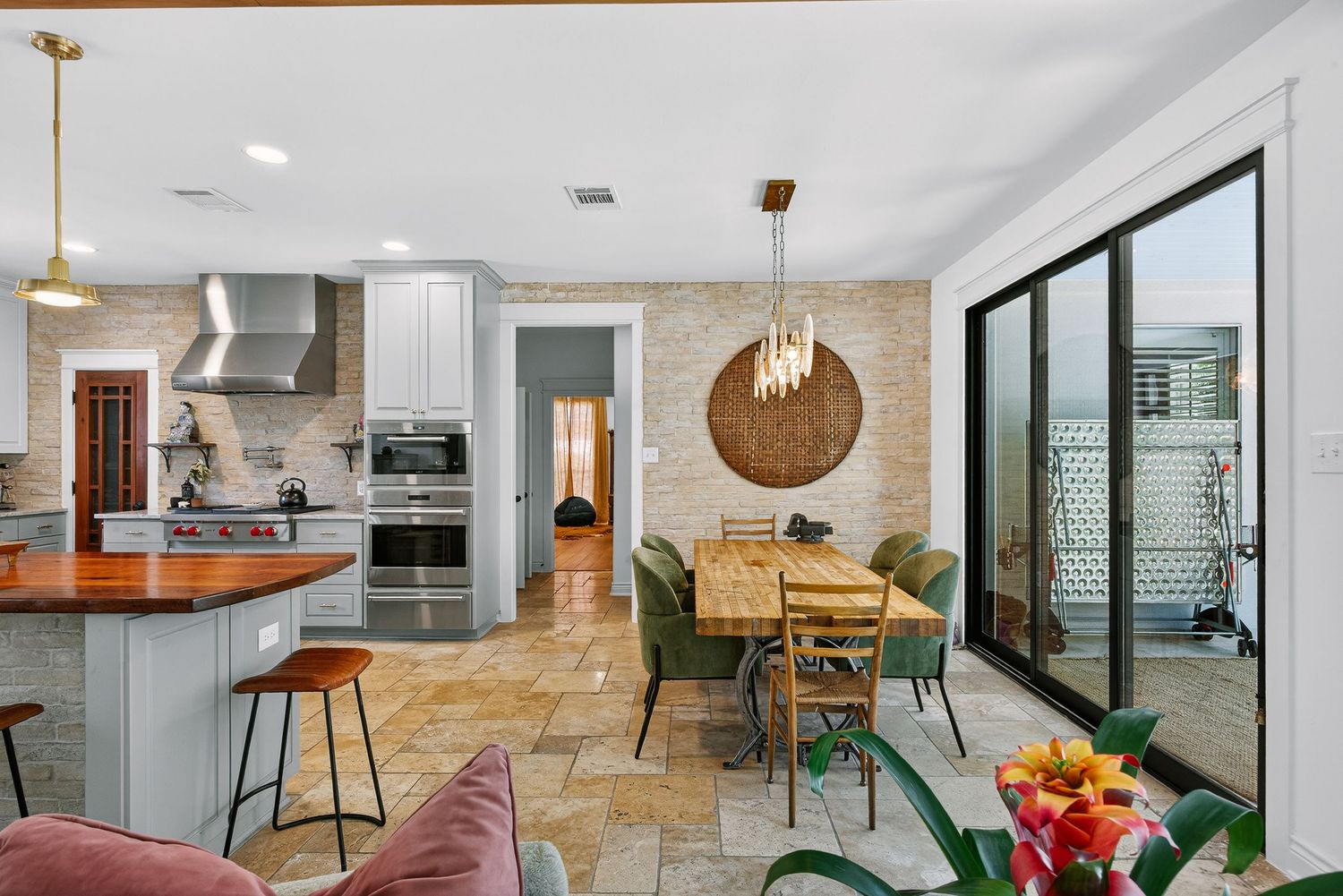 Modern open-concept kitchen and dining area with stone tile floors, wood countertops, pendant lights, and sliding glass doors.