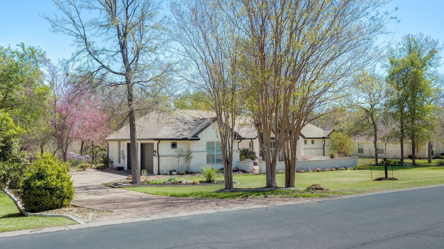 Suburban home with mature trees and manicured lawn on a quiet street during early spring.