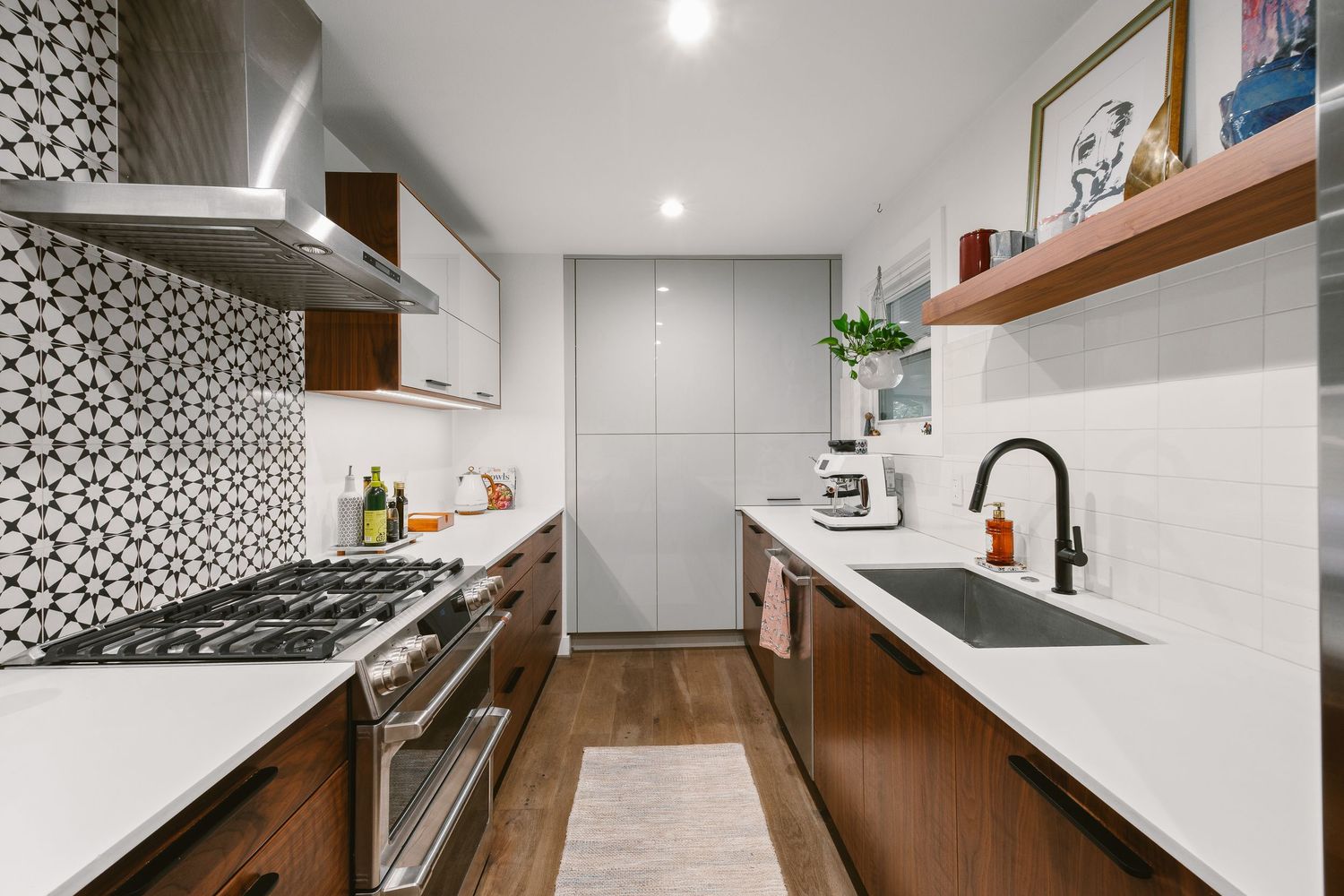 Modern galley kitchen with walnut cabinets, white quartz countertops, patterned tile backsplash, stainless steel range, and hardwood floors.