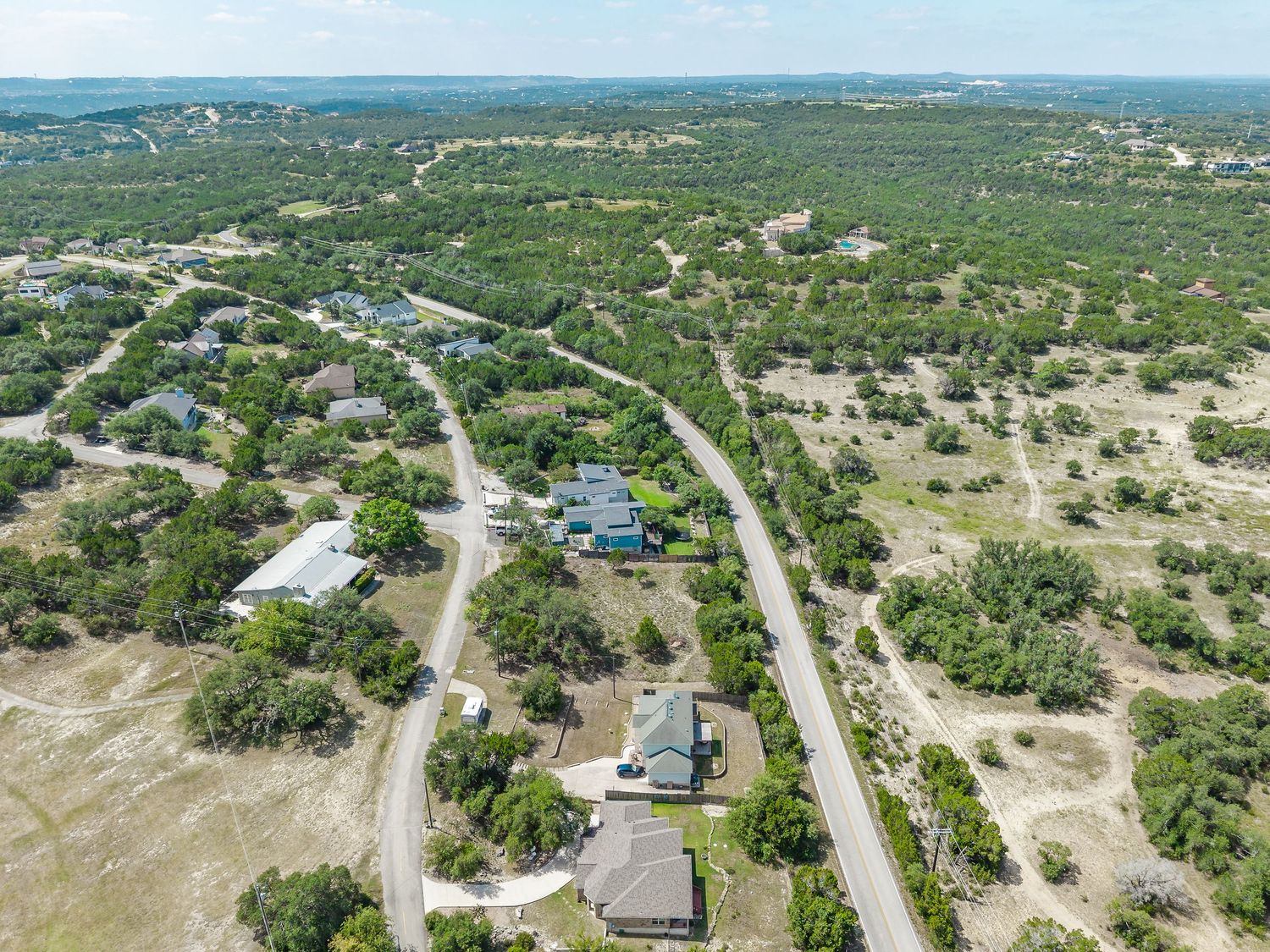 Aerial view of a rural Texas Hill Country neighborhood with scattered homes among dense oak trees and winding roads.