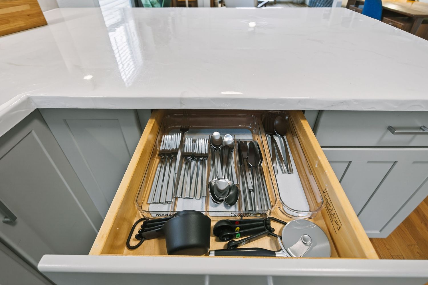 Organized kitchen drawer with neatly arranged silverware and utensils in wooden compartments.