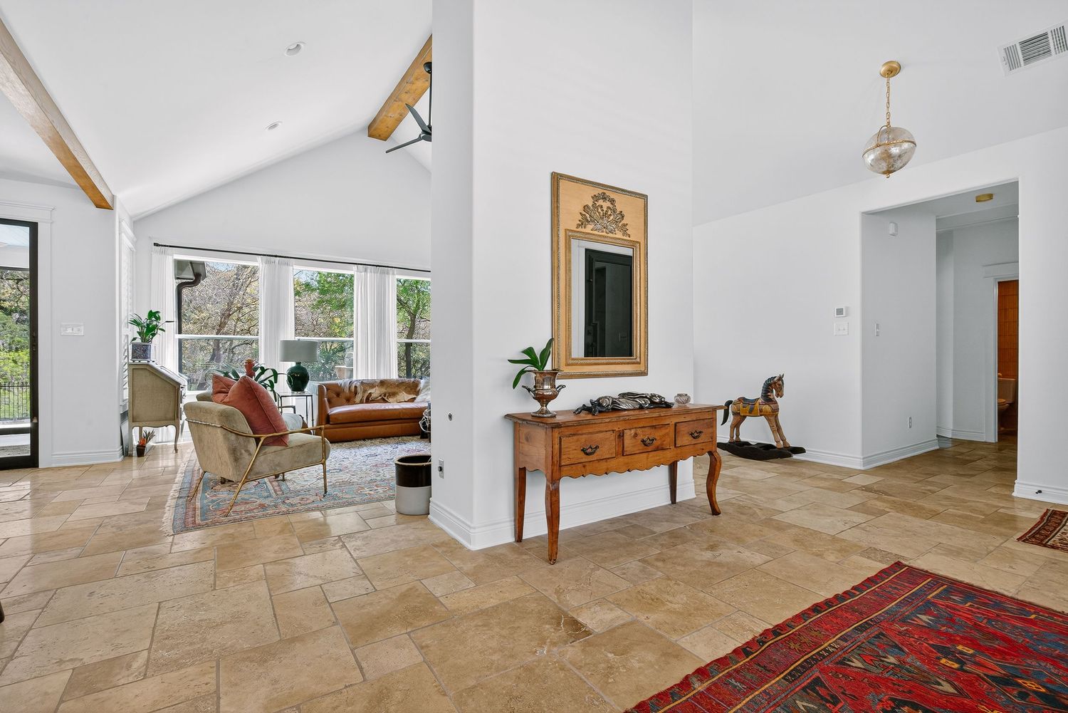 Spacious open-plan living room with vaulted ceilings, travertine tile floors, large windows, and elegant wooden console table.