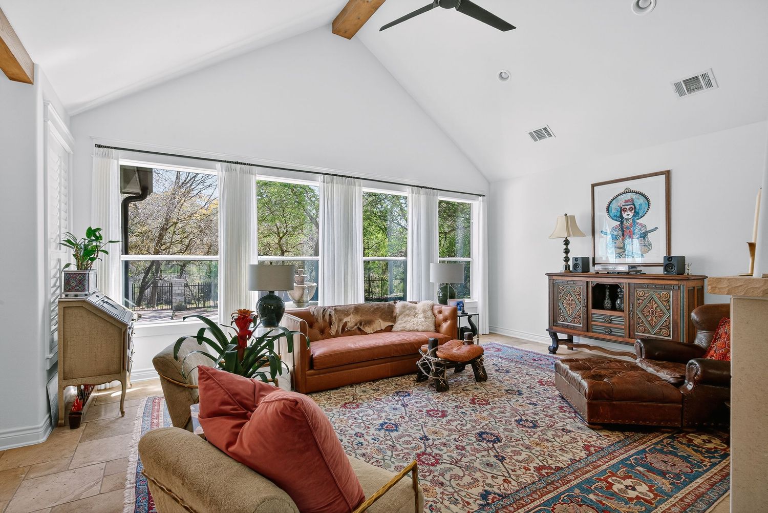 Bright living room with vaulted ceilings, exposed beams, large windows, leather sofa, colorful rug, and eclectic decor.