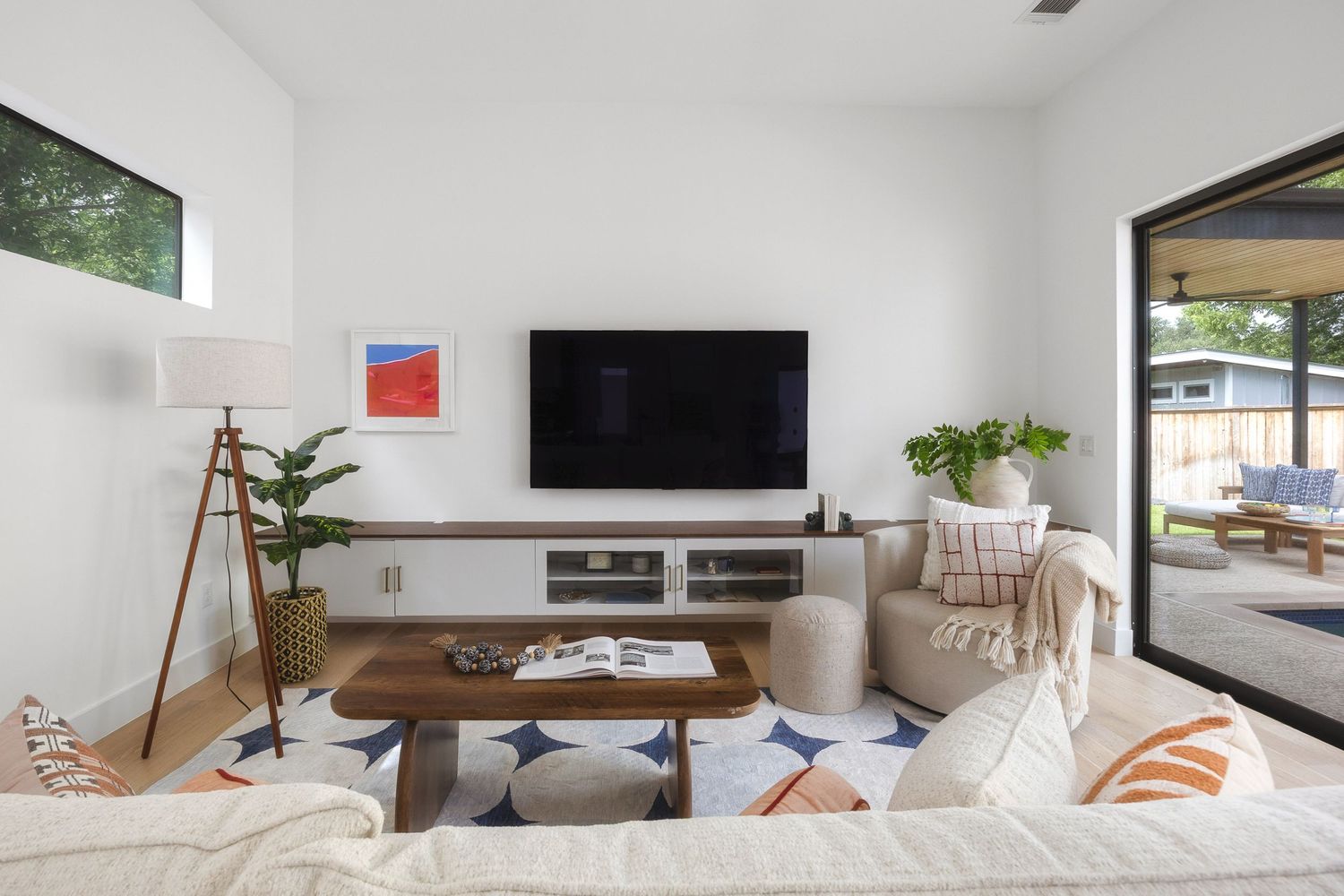 Modern white living room interior with gray sofa, wooden coffee table, and large windows letting in natural light.