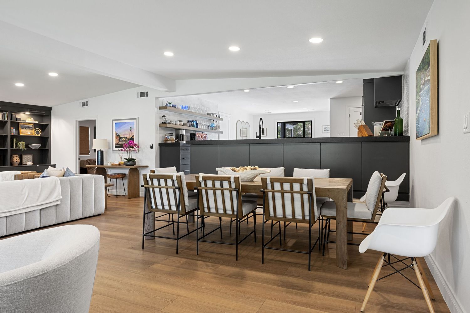 Bright dining area with wooden table, mixed chairs, open kitchen with dark cabinetry, and hardwood floors.