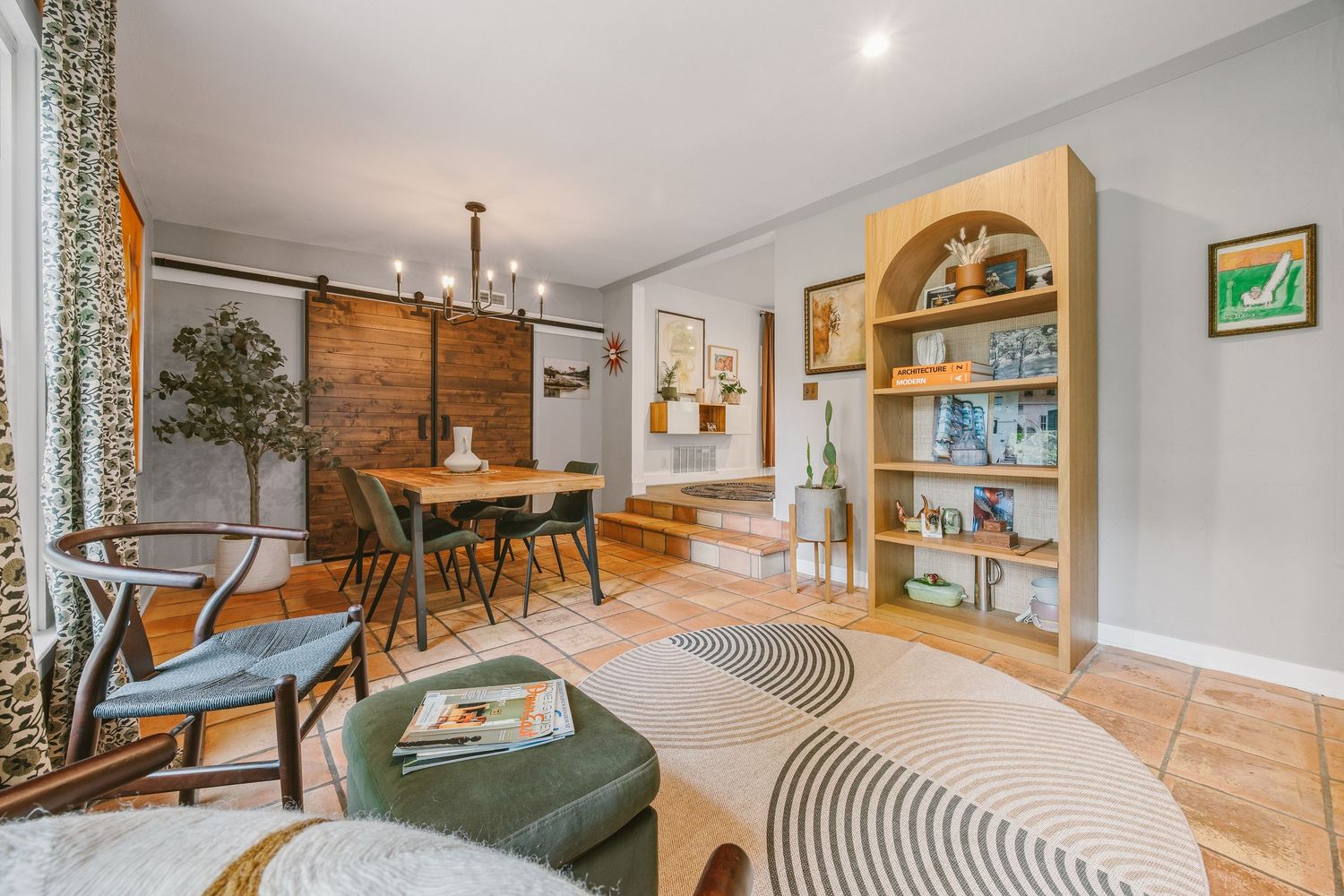 Stylish open-plan living and dining room with wooden flooring, barn door, built-in shelving, and modern pendant lighting.