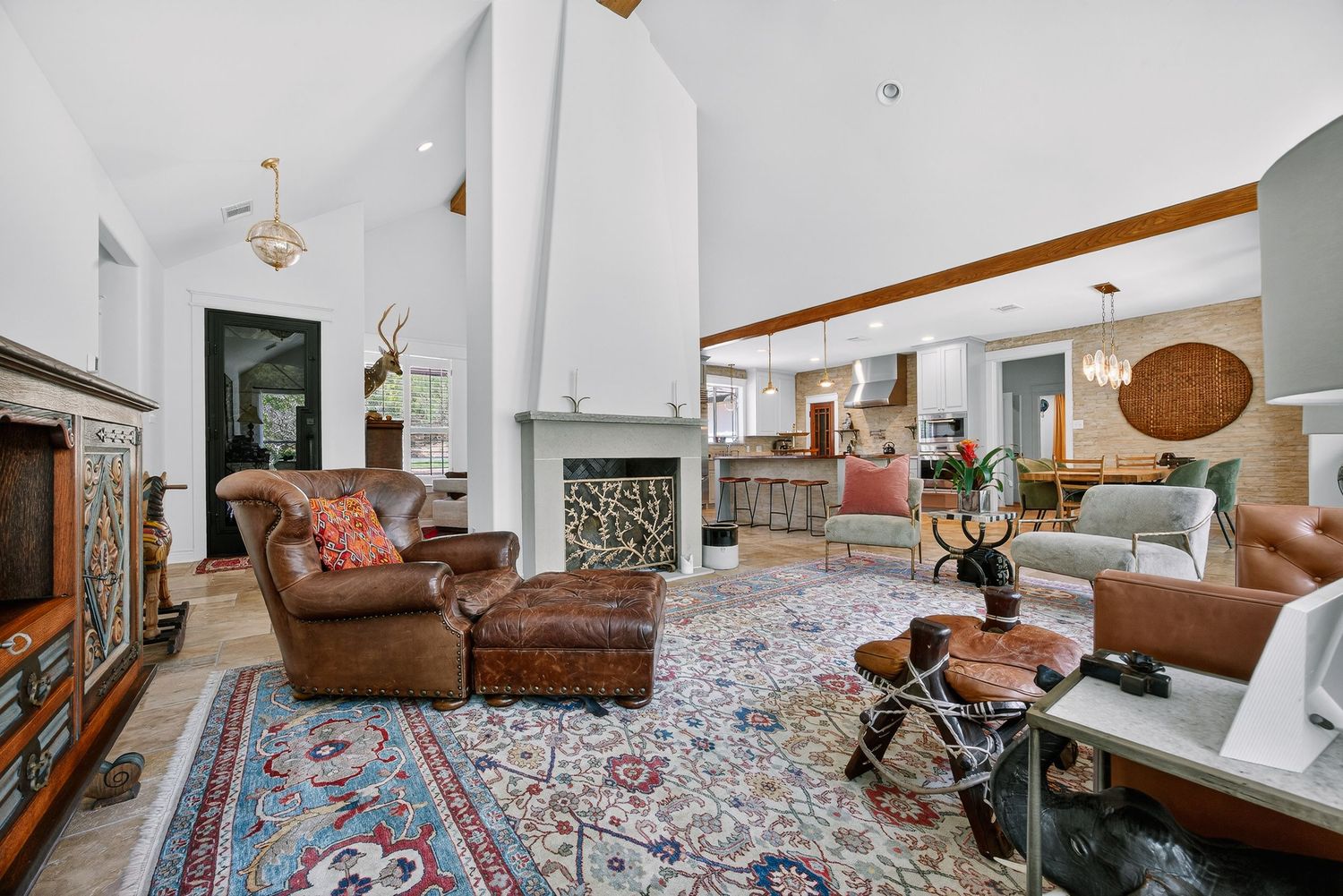 Spacious living room with vaulted ceilings, leather armchairs, ornate rug, fireplace, and open view to dining area.