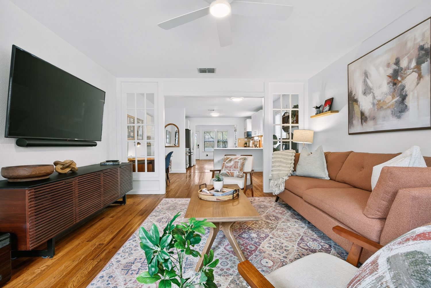 Modern living room with brown leather sofa, wood media console, and open archway leading to bright dining area.