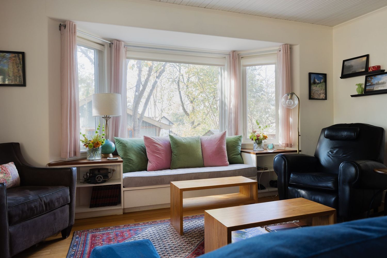 Sunlit bay window reading nook with colorful pillows flanked by leather chairs in living room setting.