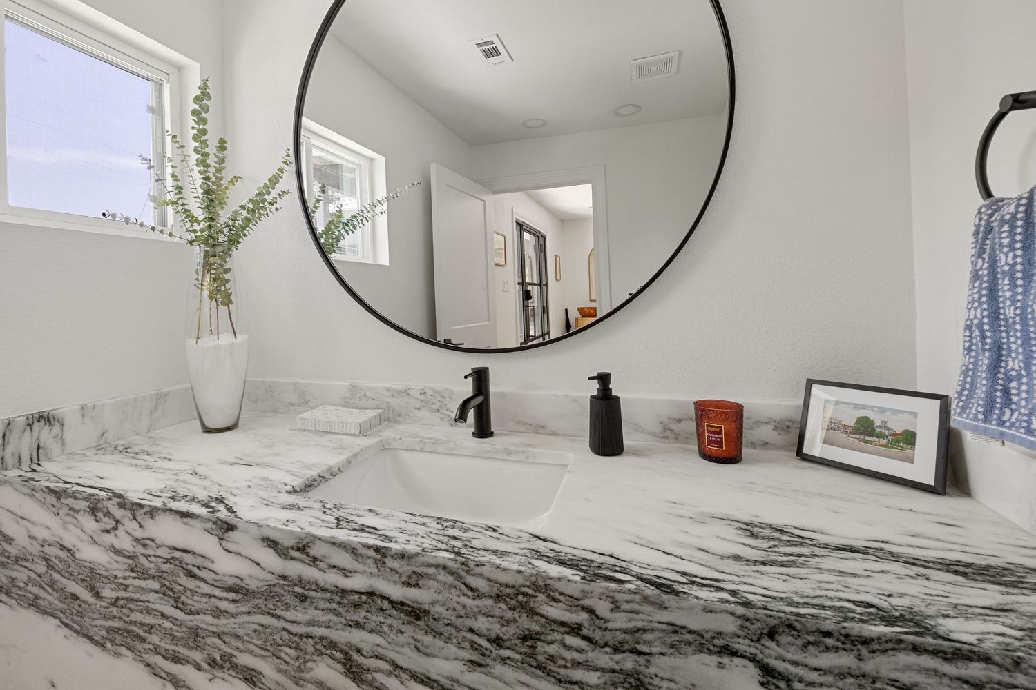 Elegant bathroom vanity with dramatic marble countertop, undermount sink, black faucet, and round mirror.