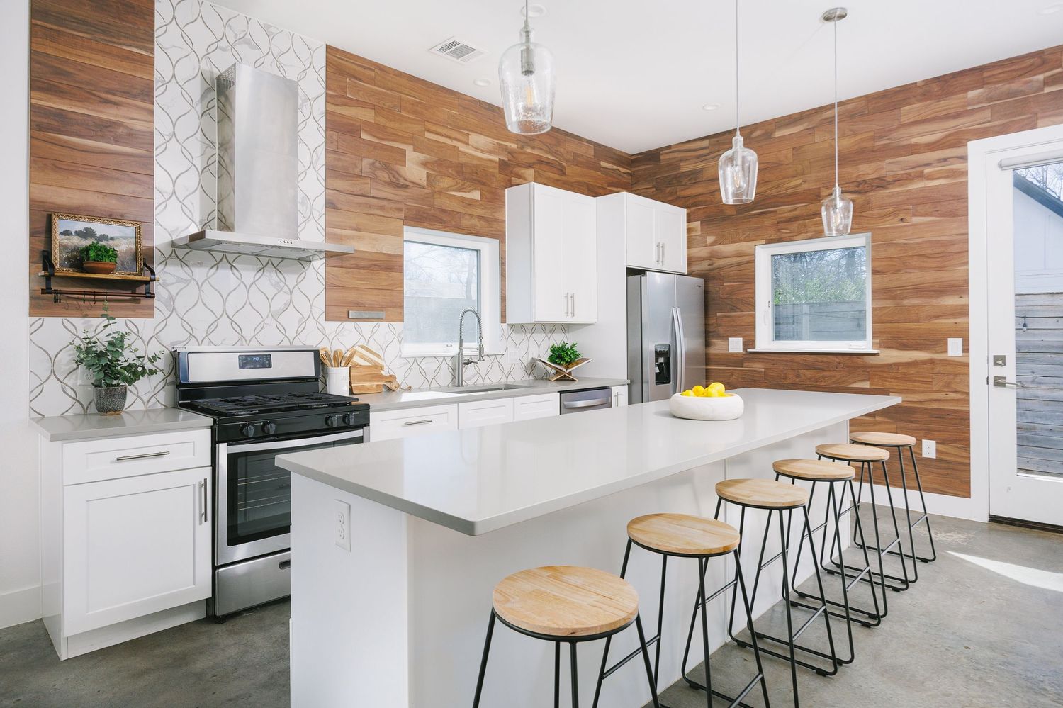 Modern white and wood kitchen design features sleek pendant lights, waterfall countertop, and minimalist bar seating.