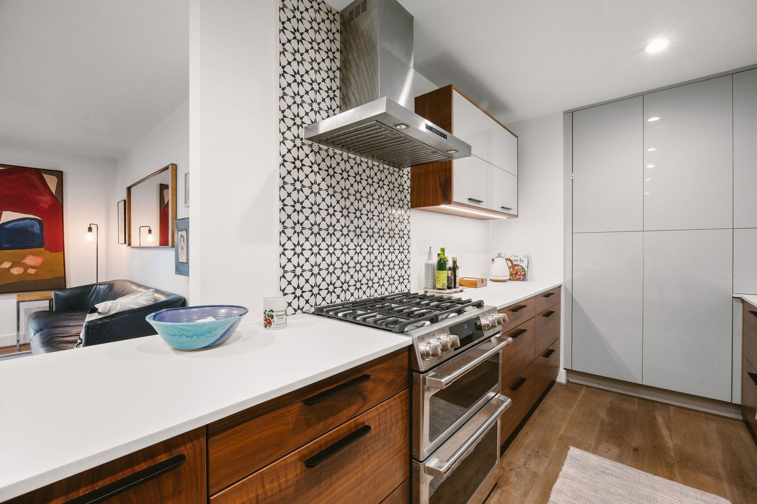 Modern kitchen with patterned tile backsplash, stainless steel range hood, gas stove, walnut cabinets, and white quartz countertop.