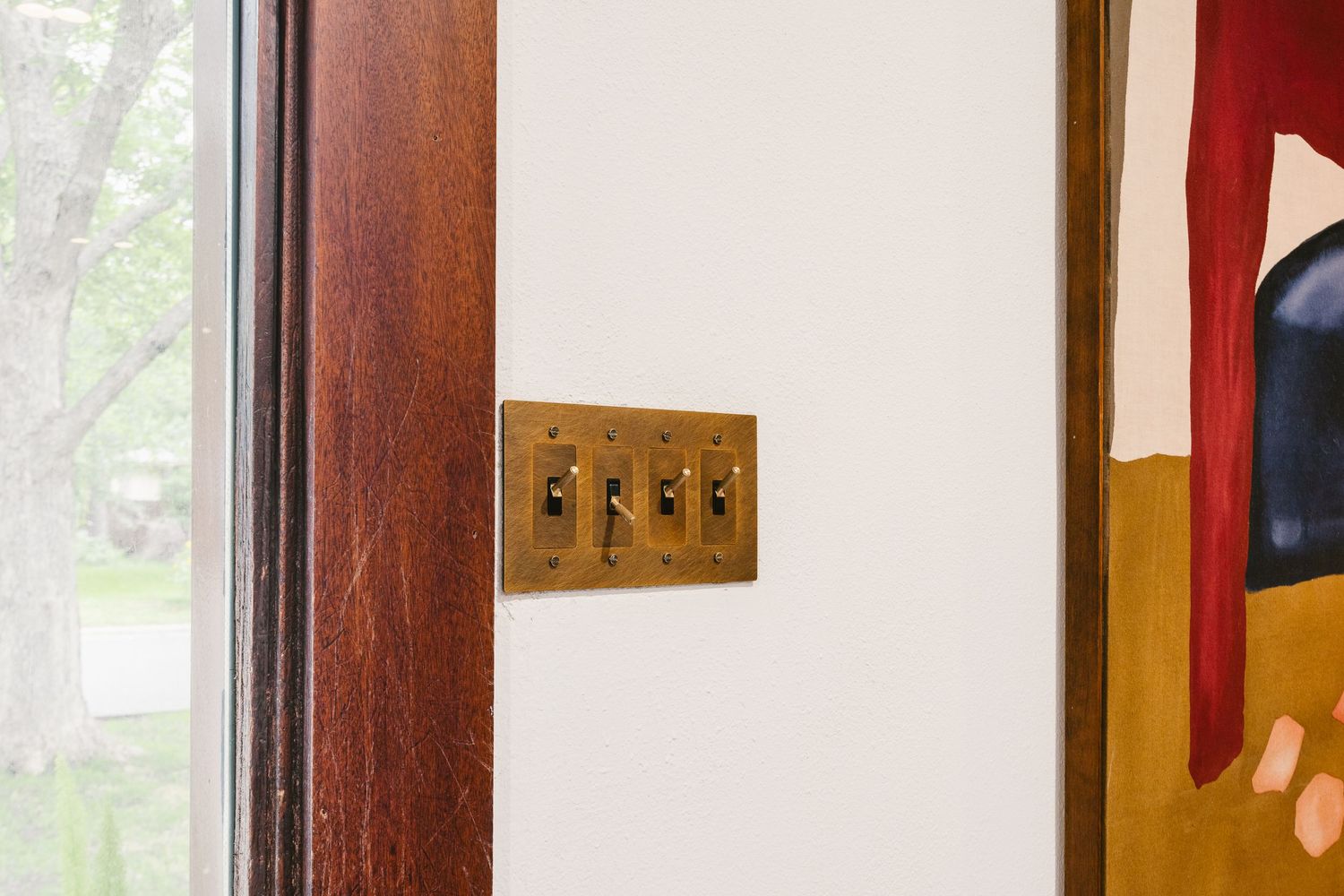 Vintage brass four-gang toggle light switch plate mounted on white wall near wooden door frame.