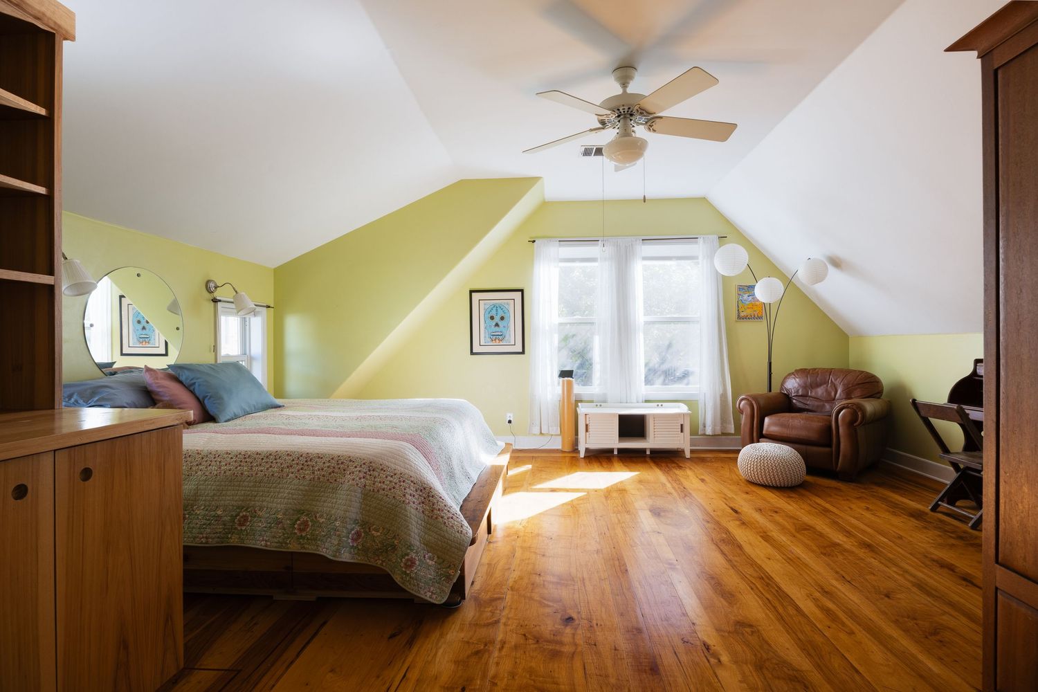 Attic bedroom with sloped ceiling, hardwood floors, and yellow-green walls.