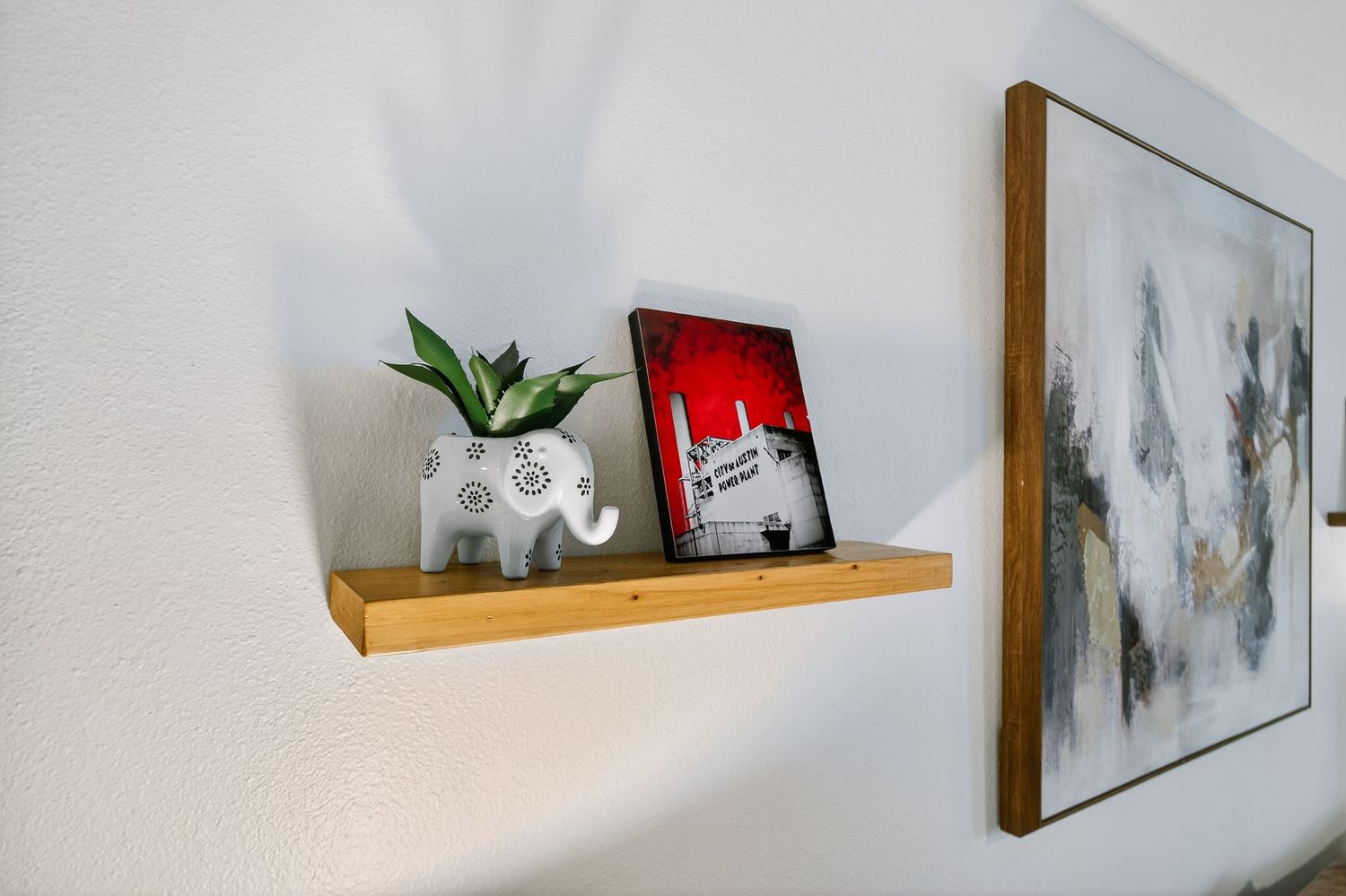 Minimalist wooden floating shelf mounted on white wall displaying decorative items and framed artwork.