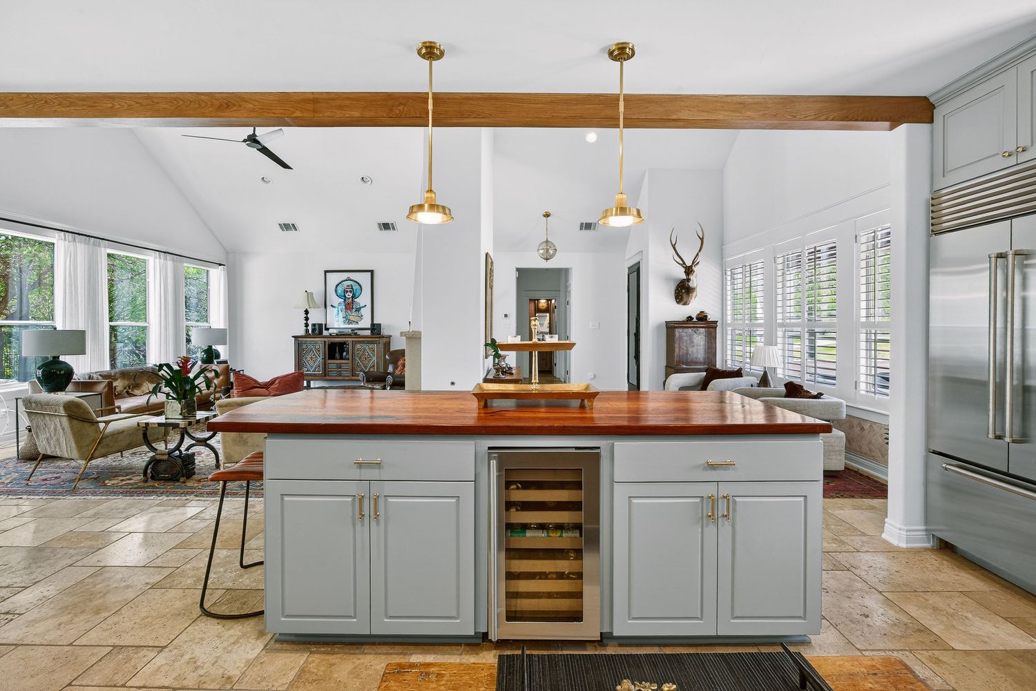 Spacious kitchen with gray island, wood countertop, wine fridge, pendant lights, and stainless steel refrigerator.