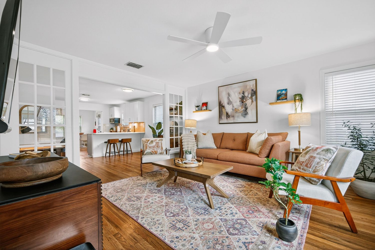 Modern living room interior with tan leather sofa, patterned area rug, and mid-century modern wood coffee table.