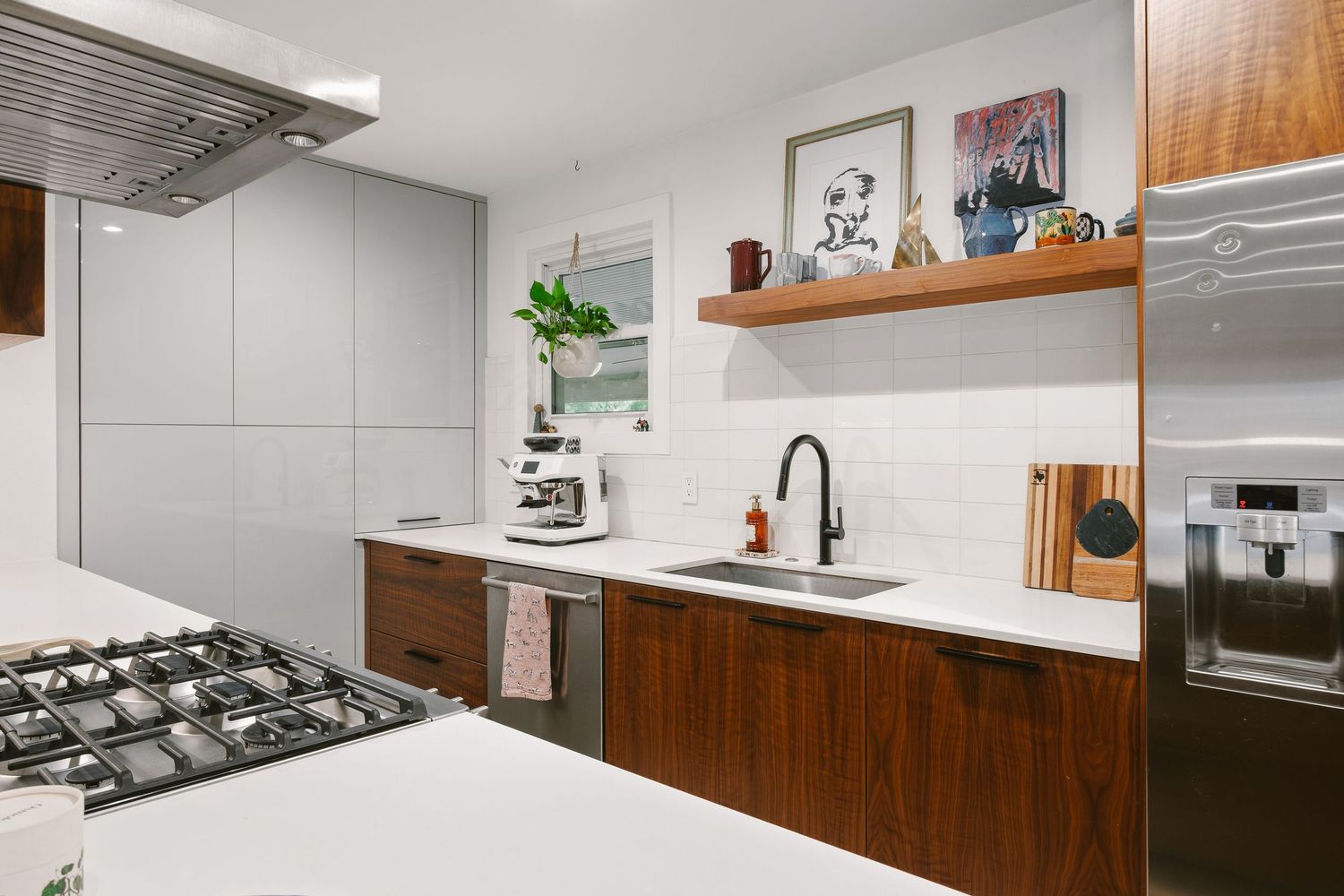 Modern kitchen with walnut cabinets, white subway tile backsplash, black faucet sink, open shelving, and stainless steel appliances.