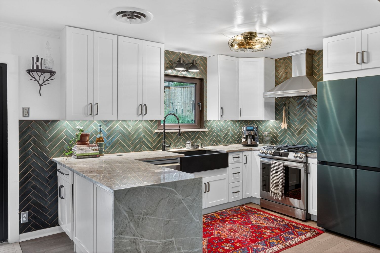 Modern kitchen with white cabinets, herringbone tile backsplash, marble island, stainless appliances, and red Persian rug.