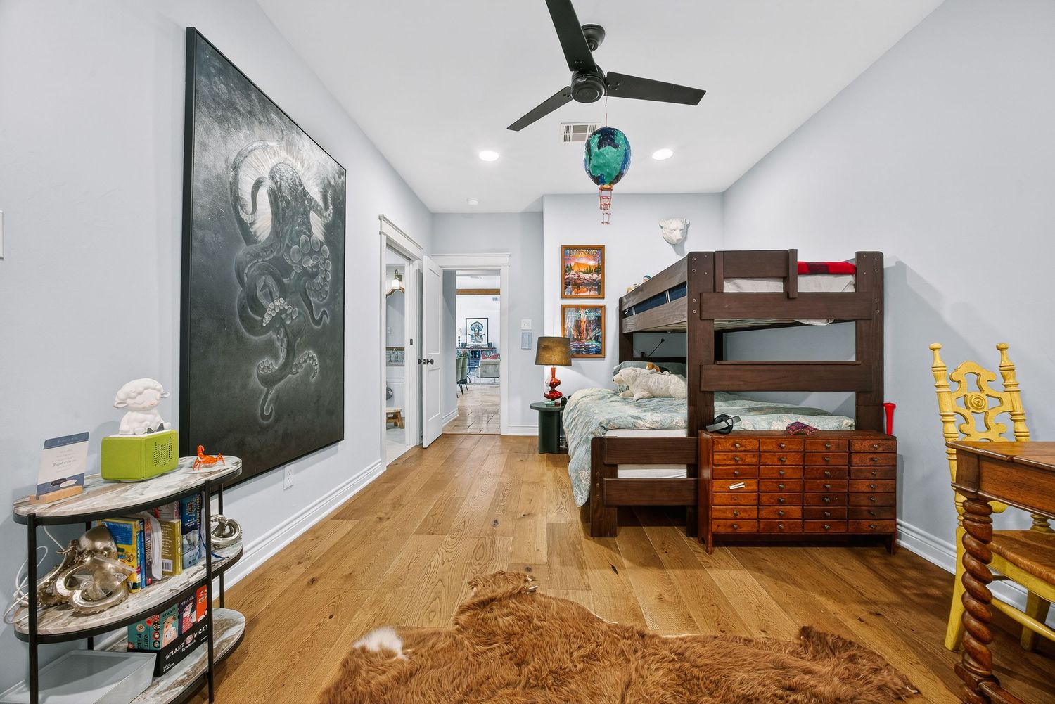 Kids bedroom with hardwood floors, bunk bed, ceiling fan, and large wall art in a bright, modern space.