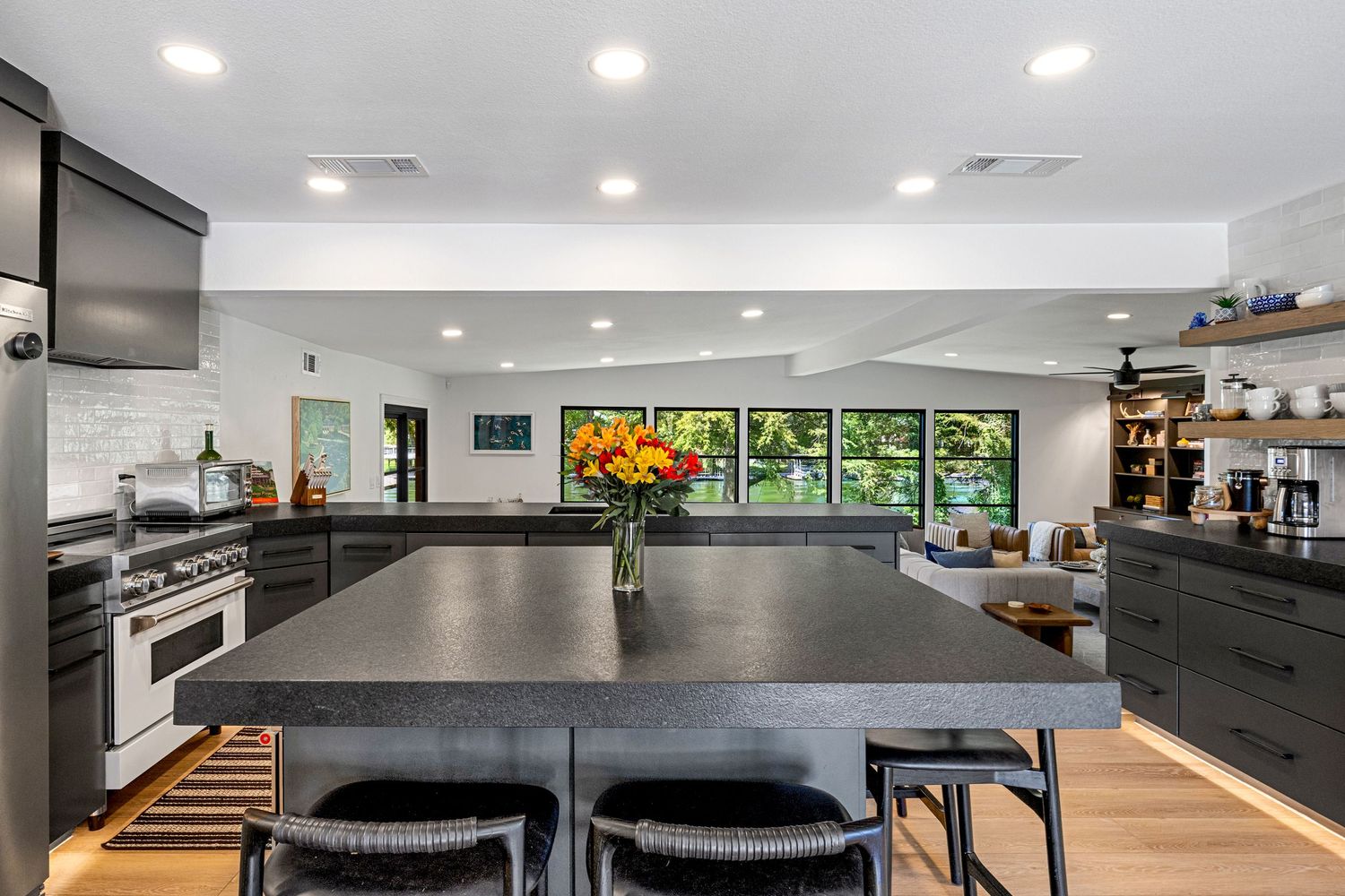 Modern kitchen with dark cabinetry, large island with bar seating, stainless steel range, and views of lush greenery.