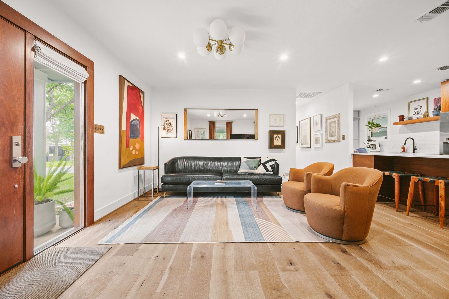 Modern living room with light hardwood floors, leather sofa, cognac chairs, striped rug, and bar area in background.