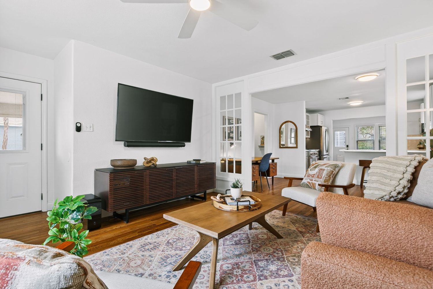 Modern white living room with hardwood floors, mounted TV, and natural light streaming through multiple windows.