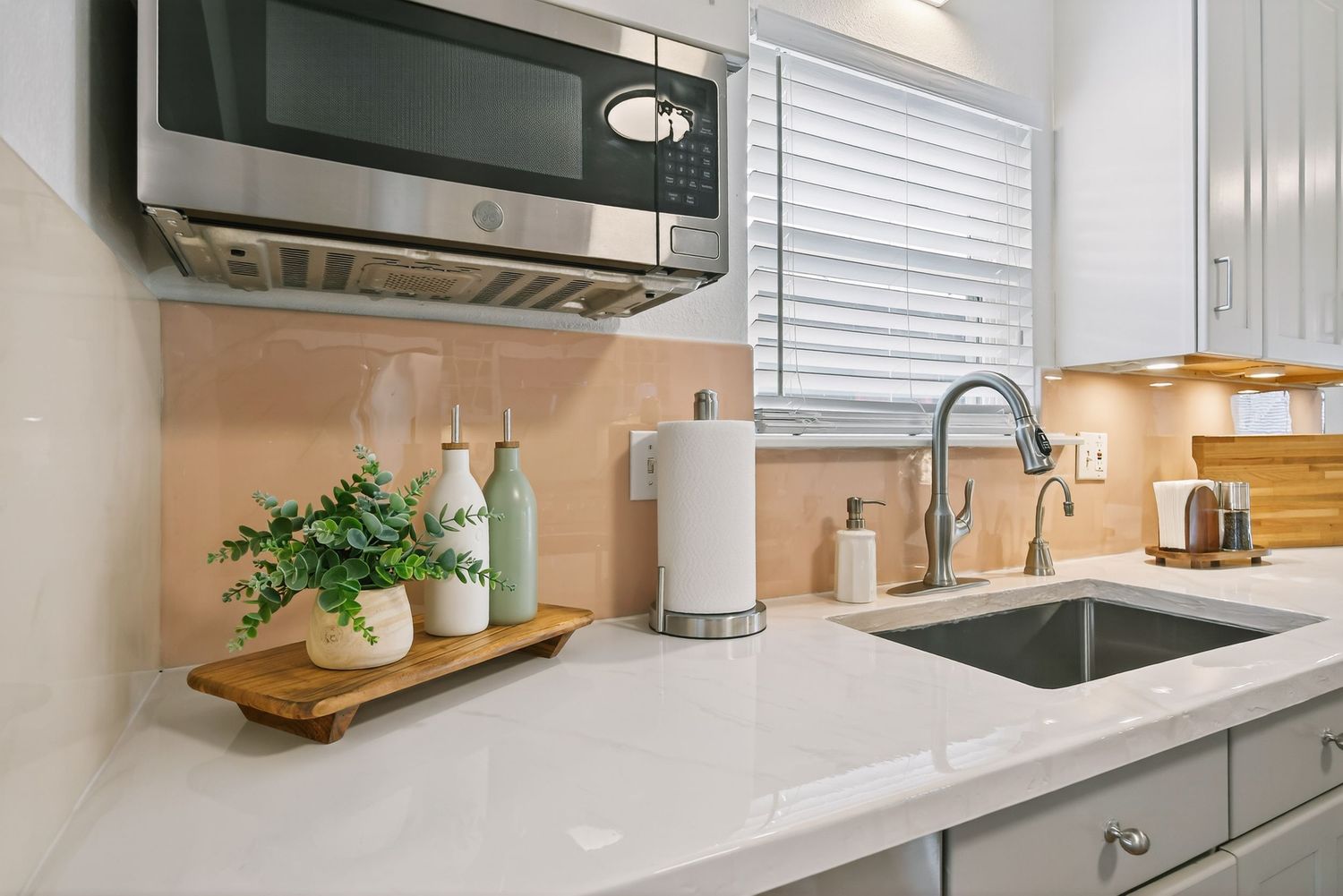 Modern white kitchen interior with wood accents, floating shelves, and stainless steel appliances.