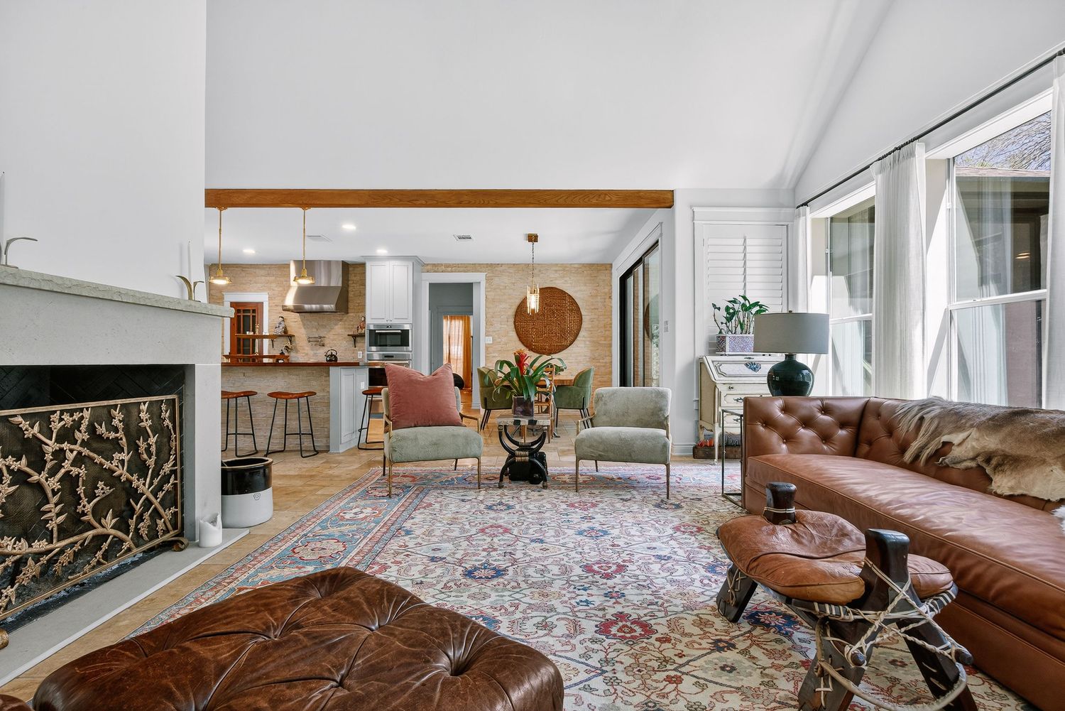 Elegant living room with leather sofa, ornate rug, fireplace, vaulted ceilings, and open view to kitchen beyond.