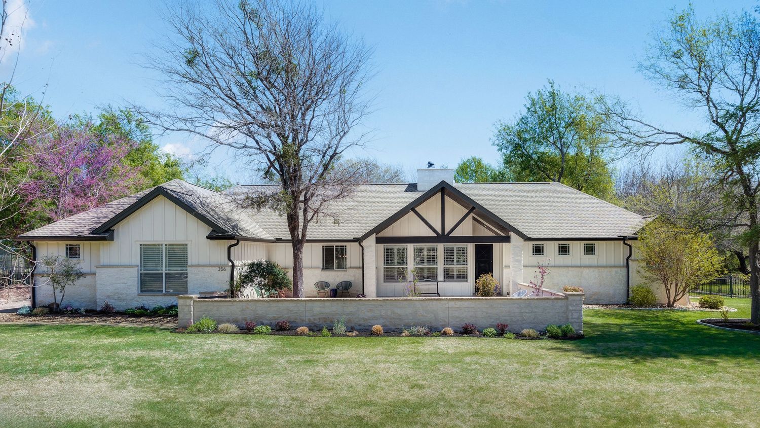 Ranch-style home with white brick exterior, gabled roof, large lawn, and colorful spring trees in a serene suburban setting.