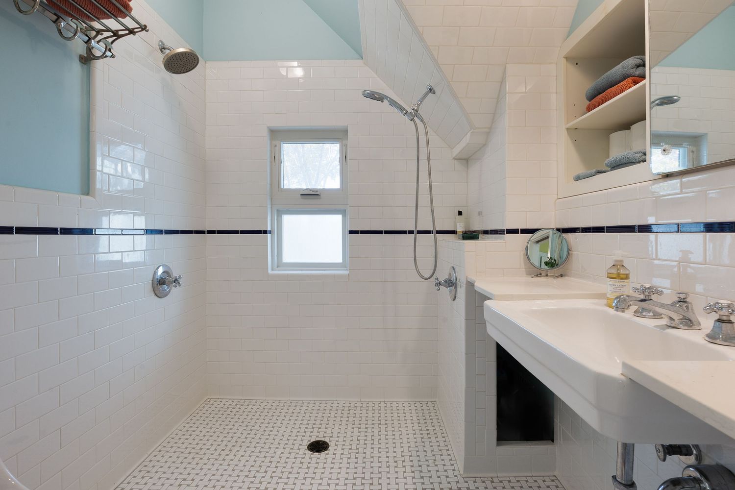 Clean white bathroom with tiled shower, built-in shelving, and natural light from window.