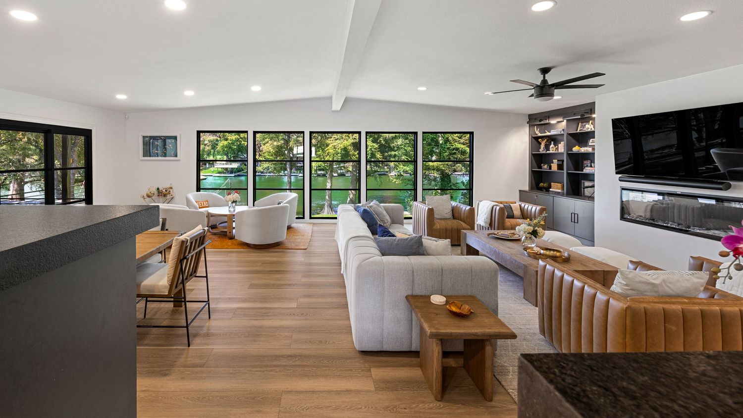 Spacious open-plan living area featuring vaulted ceilings, mixed seating, hardwood floors, and panoramic garden-view windows.